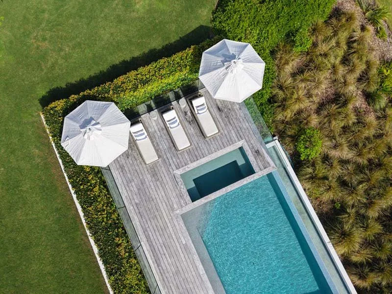 Aerial view of a backyard with a swimming pool, two white umbrellas, lounge chairs, and surrounding greenery.