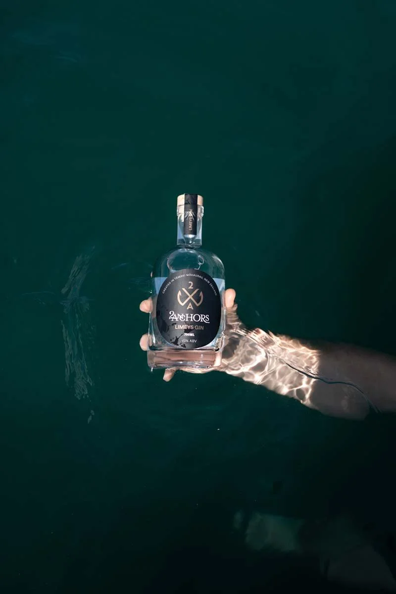 Person holding a bottle of Anchors Limey’s Gin underwater in a dark body of water.