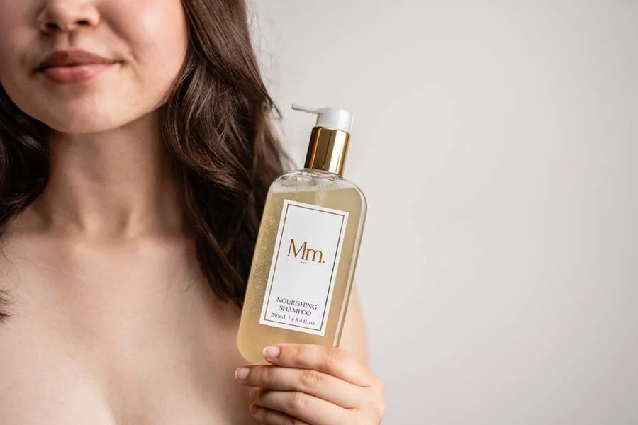 A woman holding a bottle of nourishing shampoo with a gold and white label.
