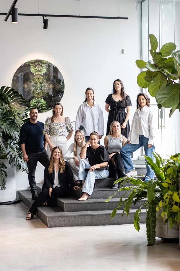 Group of nine diverse people posing on staircase with greenery and modern interior background.