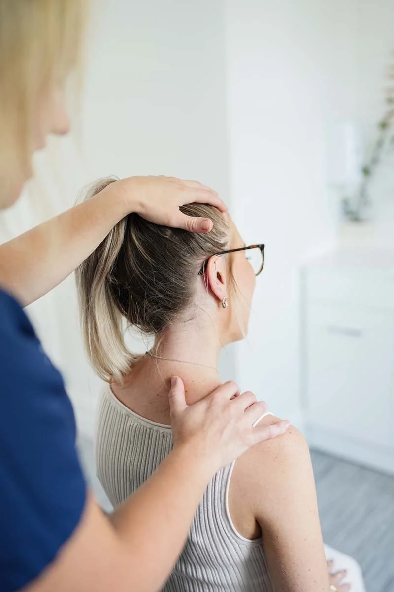 A person receiving a neck massage or chiropractic adjustment from a therapist in a bright, clean room.