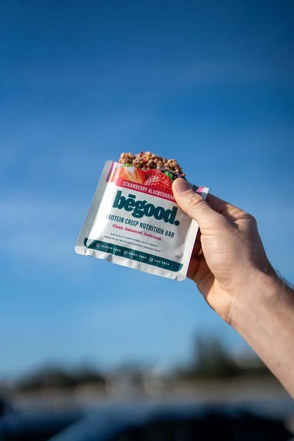 A hand holding a packaged protein bar with a blue sky background.
