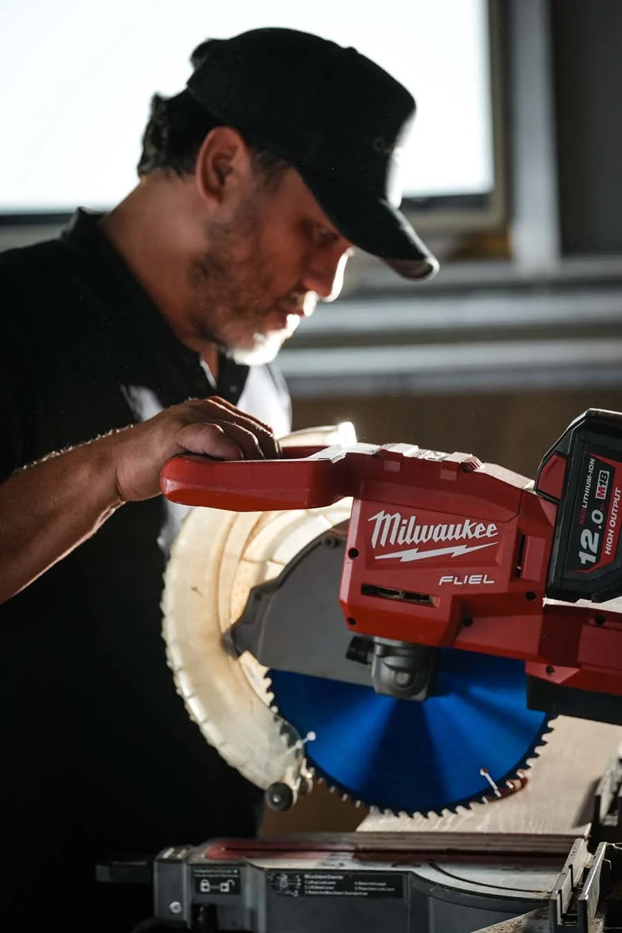 A man using a red Milwaukee miter saw with a blue blade to cut wood.