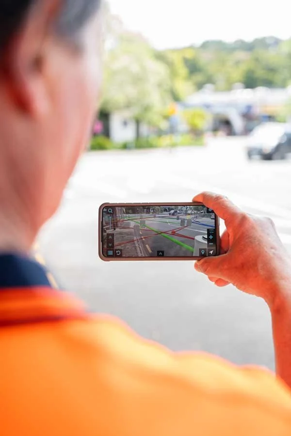 A person viewed from behind is holding a smartphone and taking a picture of a parking lot with a truck and a car, possibly for surveillance or parking assistance.