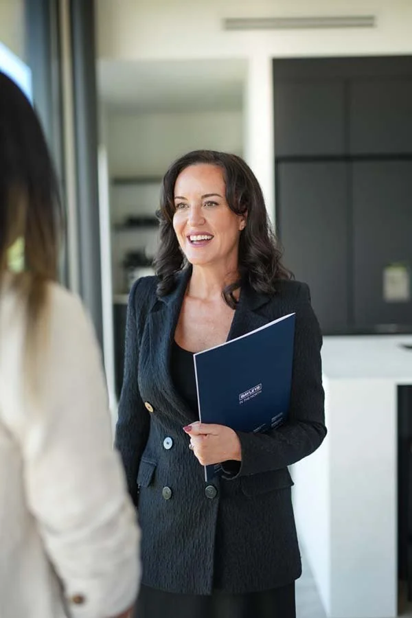 Woman speaking to another person, holding a folder, in a modern office setting.