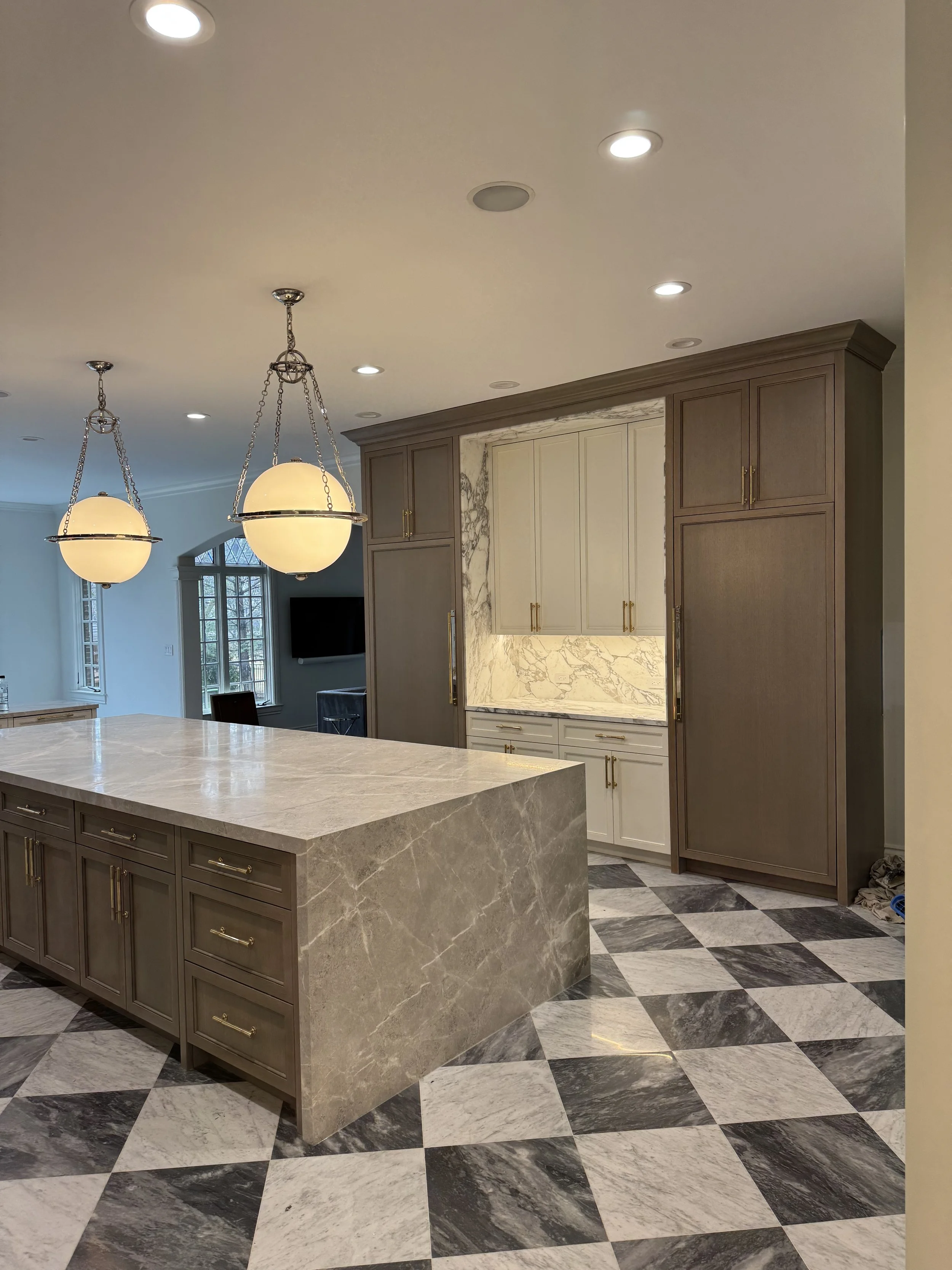 Modern kitchen with marble and dark wood accents, featuring a marble island, checkered black and white marble flooring, and pendant lighting.
