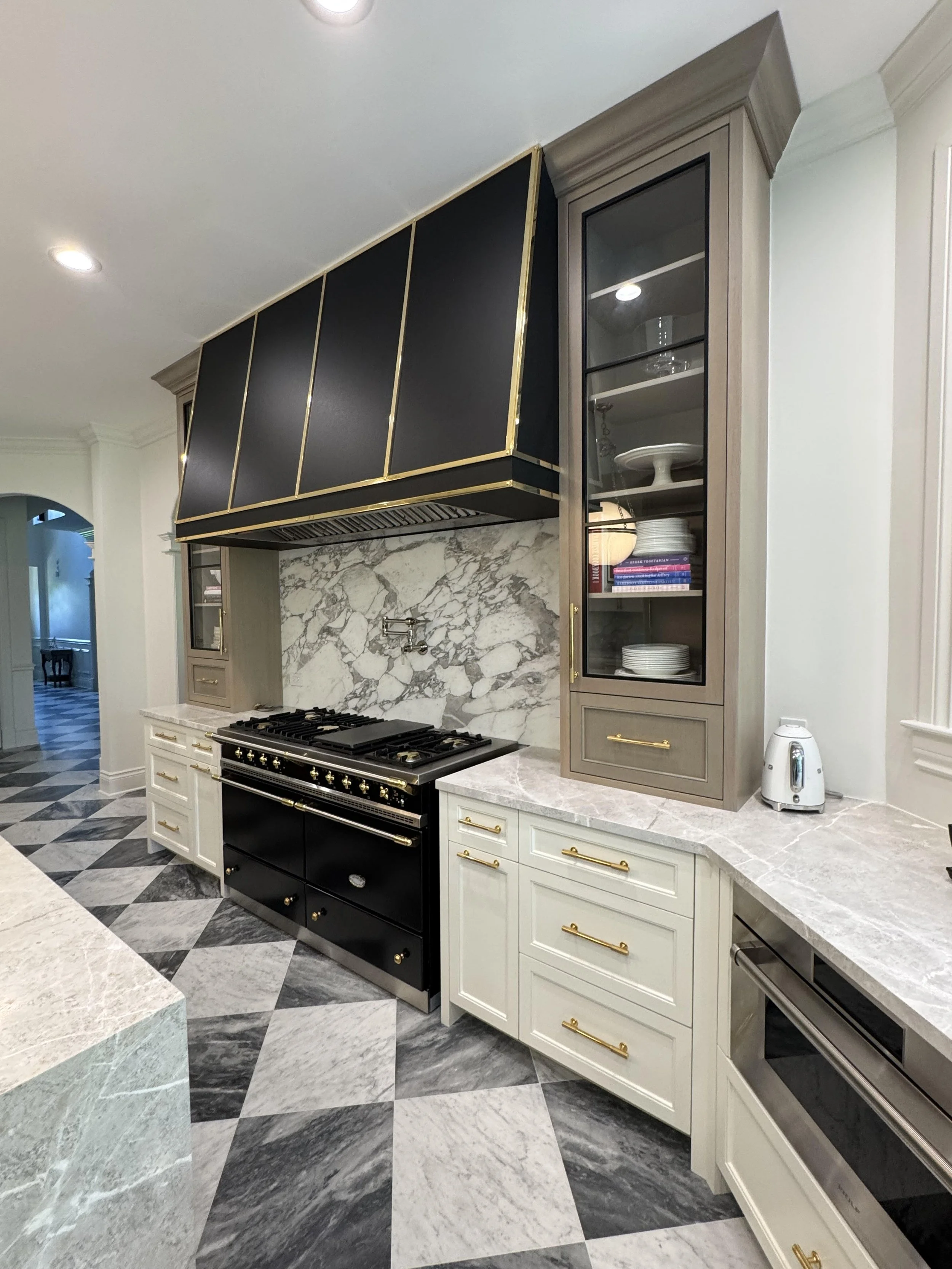 Kitchen with black and gold range, white cabinets with gold handles, marble backsplash, glass-front cabinet, and checkered floor.