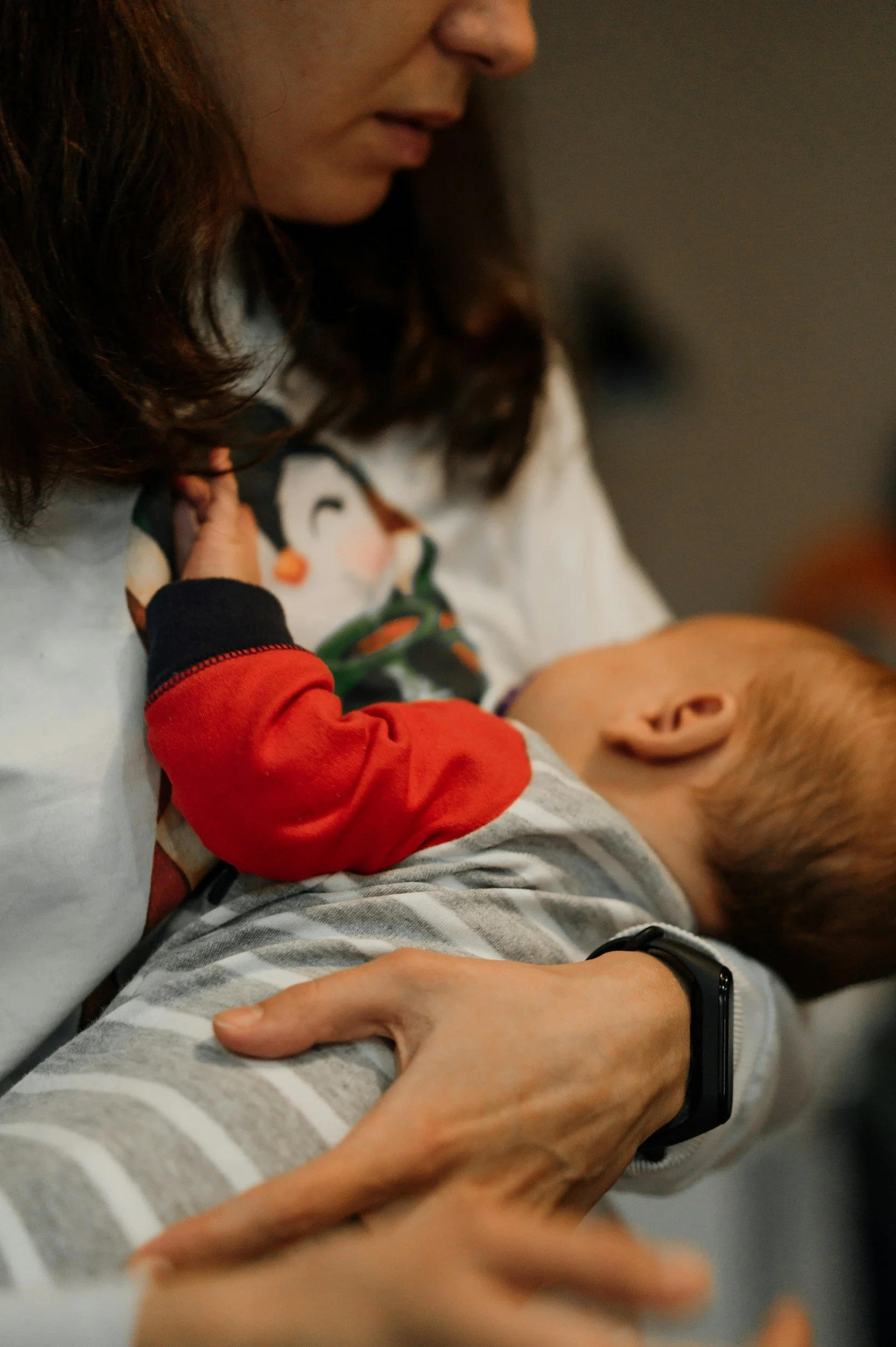 A woman holding a sleeping baby close to her chest, with her arm around the baby's back, in a cozy indoor setting Lactology Sunshine Coast.