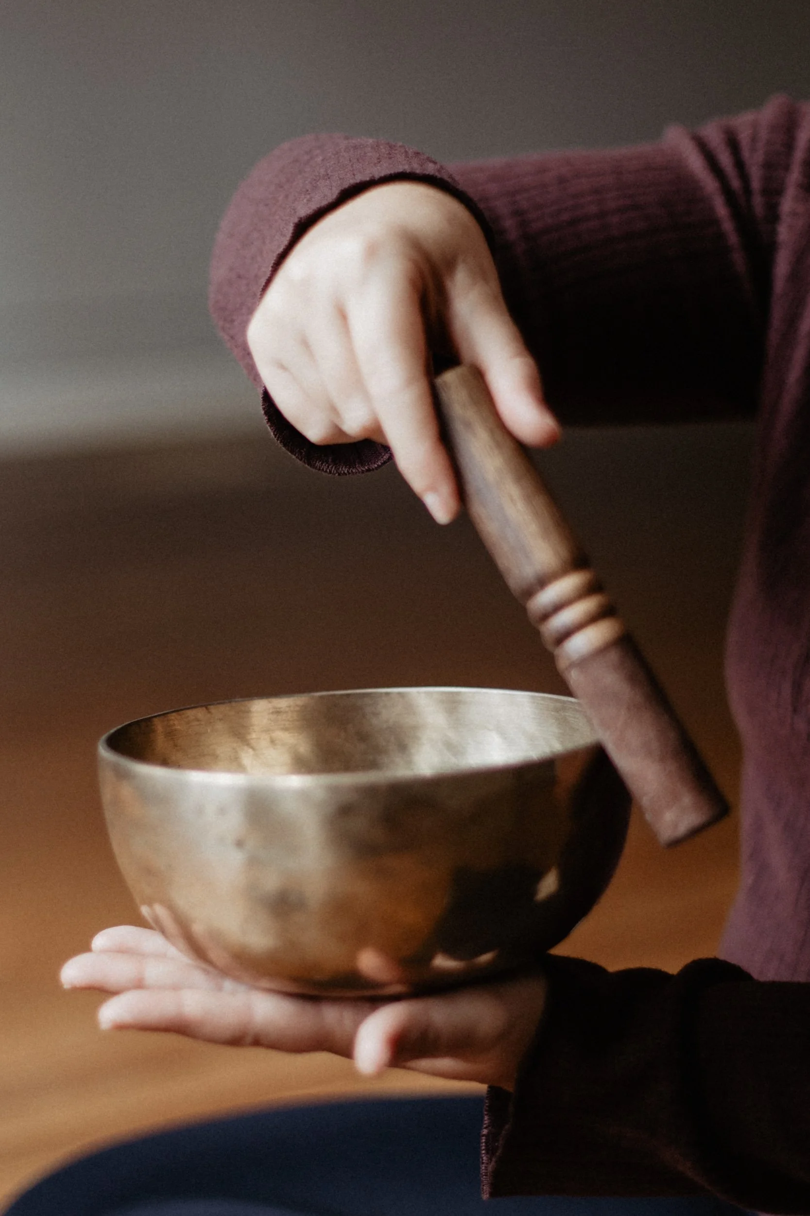 Person holding a wooden stick and a metallic bowl with a blurred background.