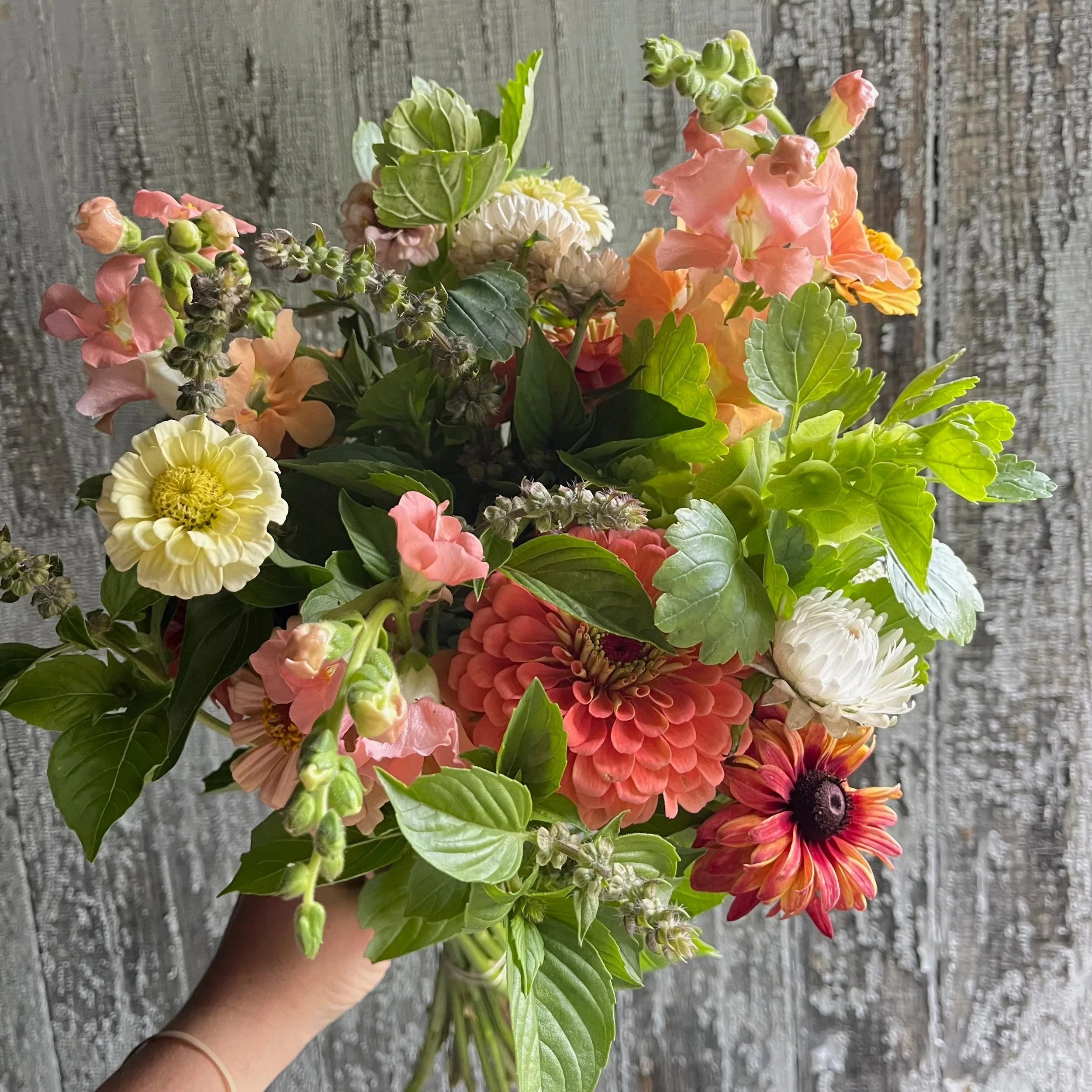 A hand holding a colorful bouquet of mixed flowers against a rustic wooden background.