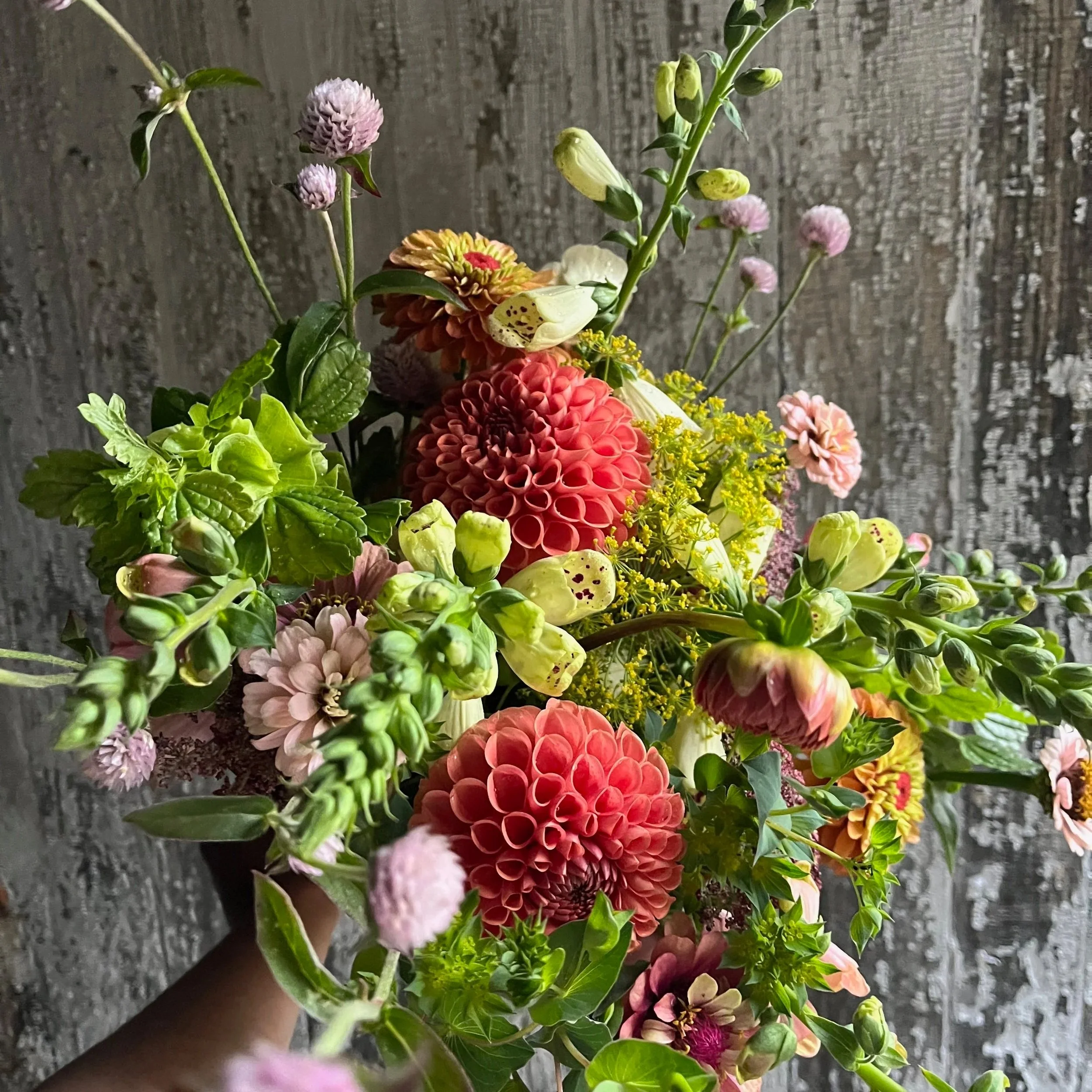 A colorful bouquet of various flowers including dahlias, zinnias, and other colorful blooms against a rustic wooden background.