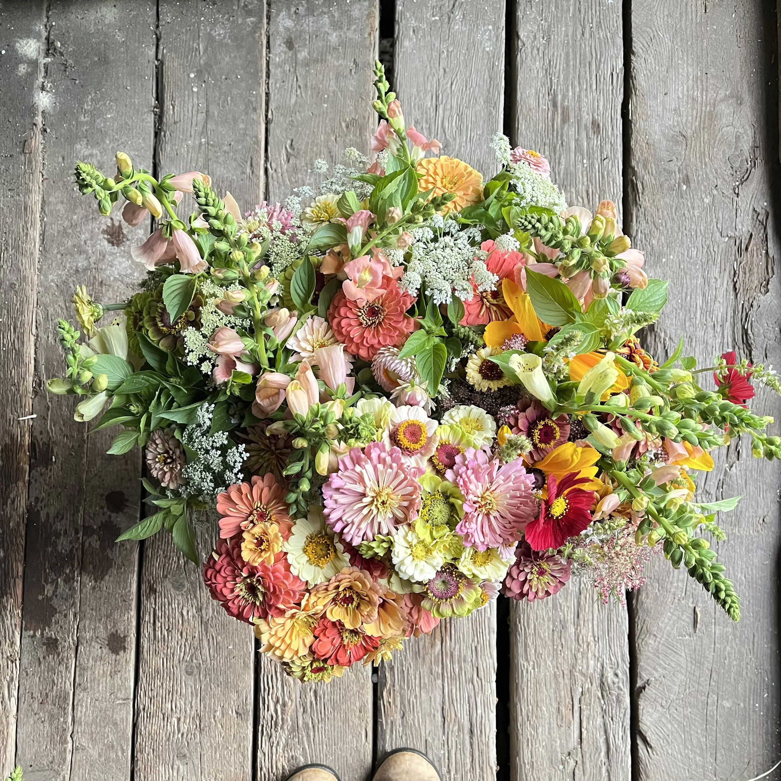 Colorful bouquet of various flowers including pink, yellow, white, and red blossoms, arranged on a rustic wooden surface.