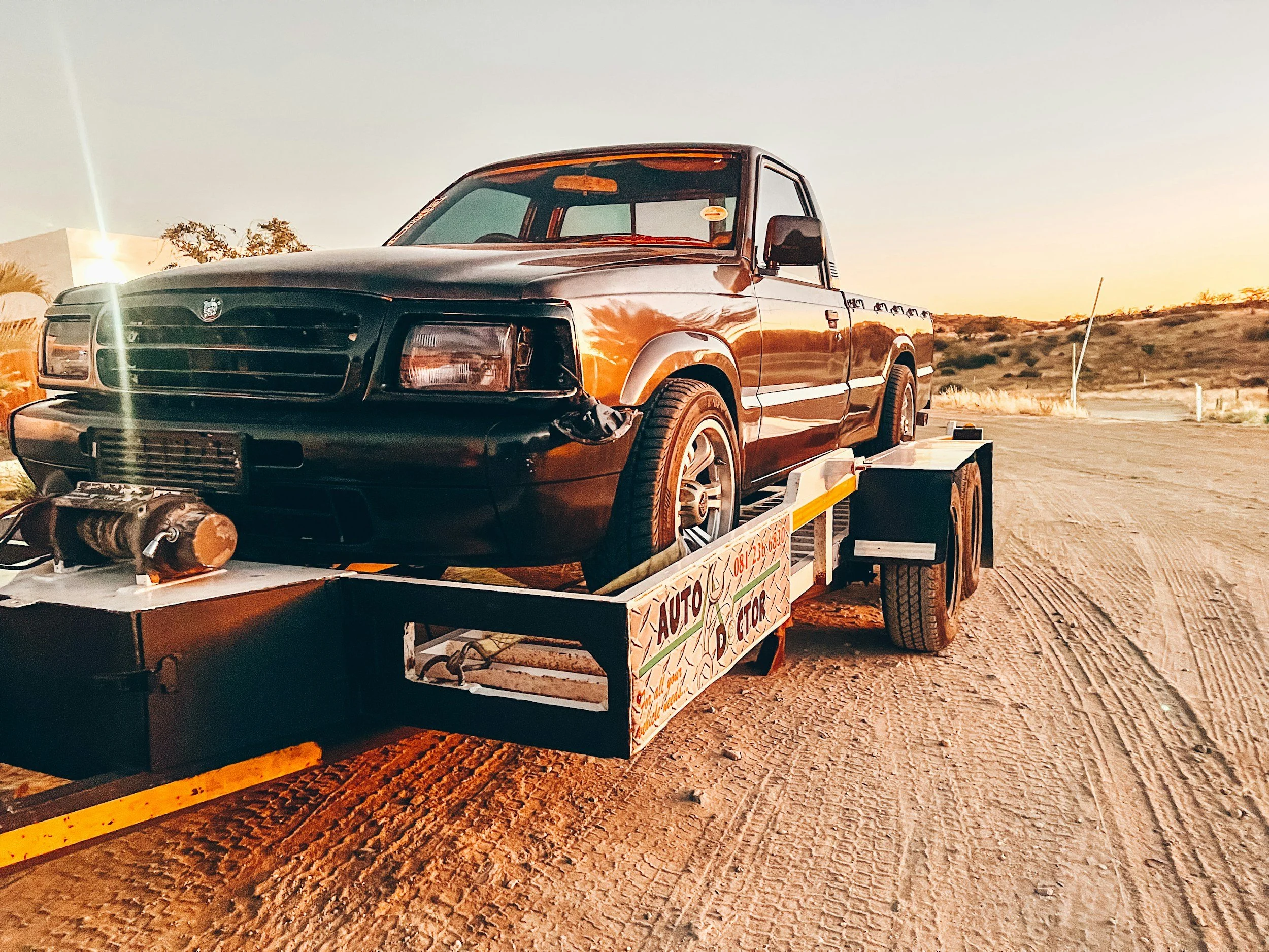 A black pickup truck loaded onto a flatbed trailer in a desert landscape during sunset.