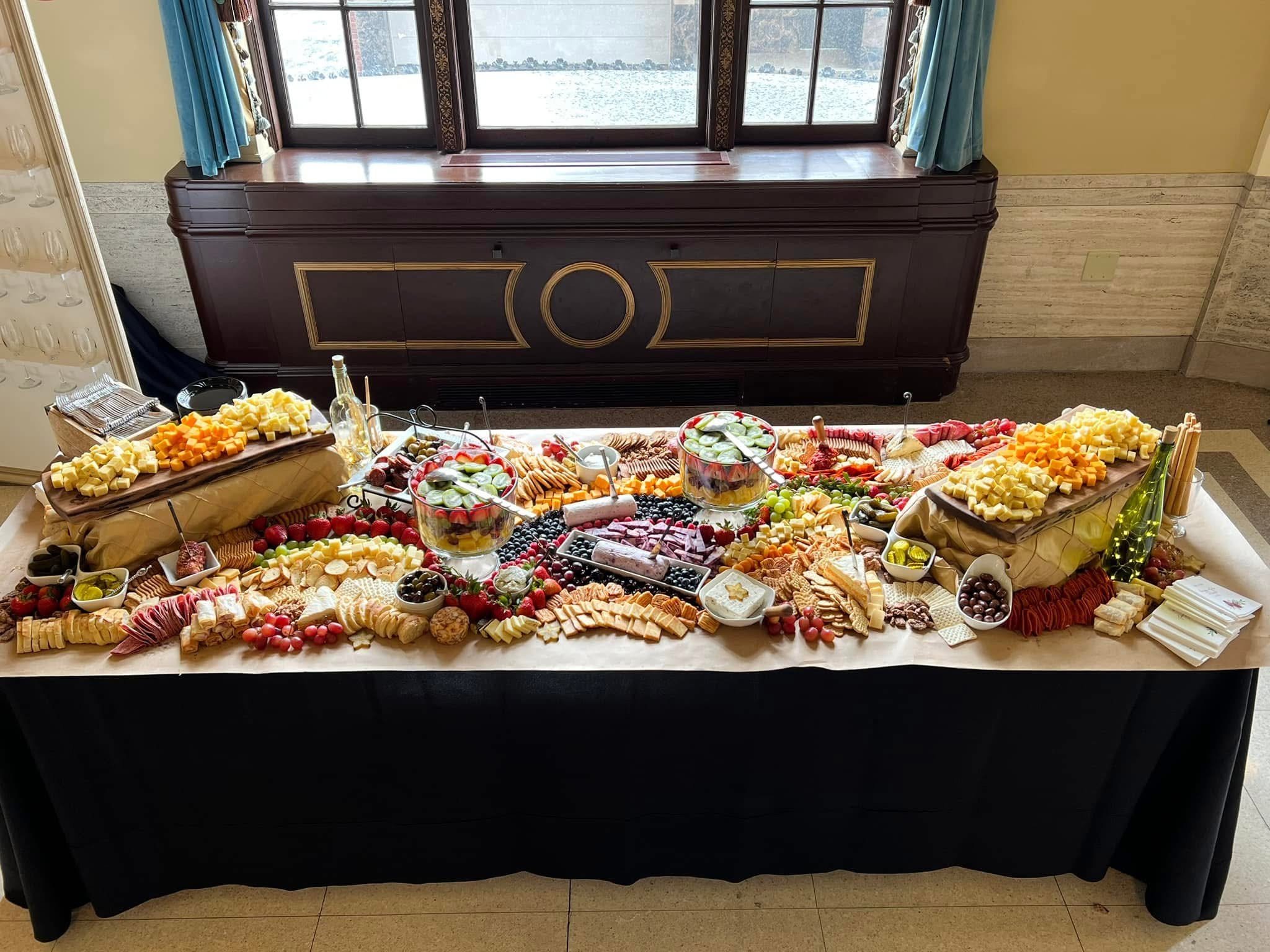 Cheese, crackers, grapes, strawberries, and other snacks arranged on a buffet table with a window in the background.