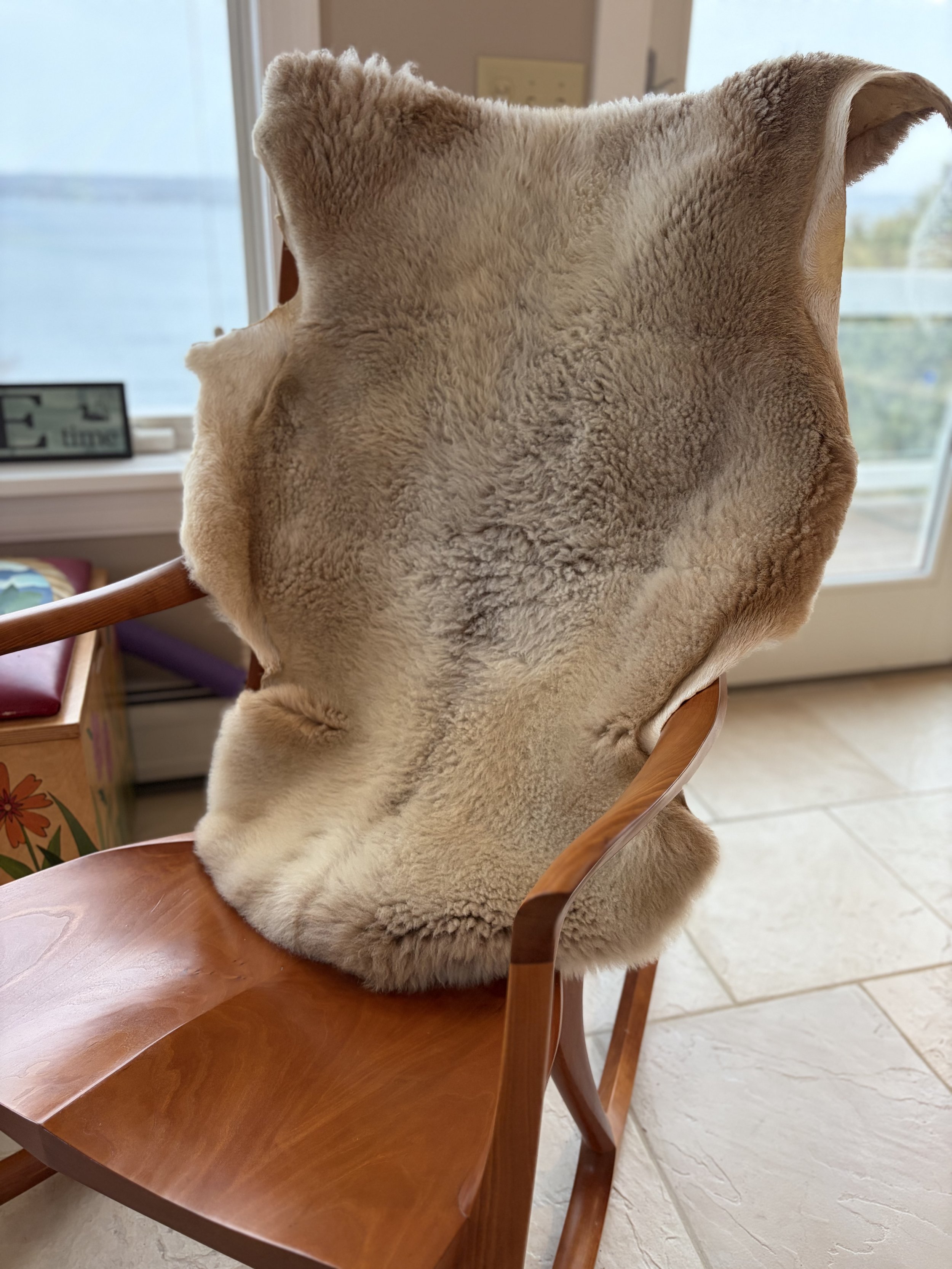 A wooden chair with a sheep skin draped over it.