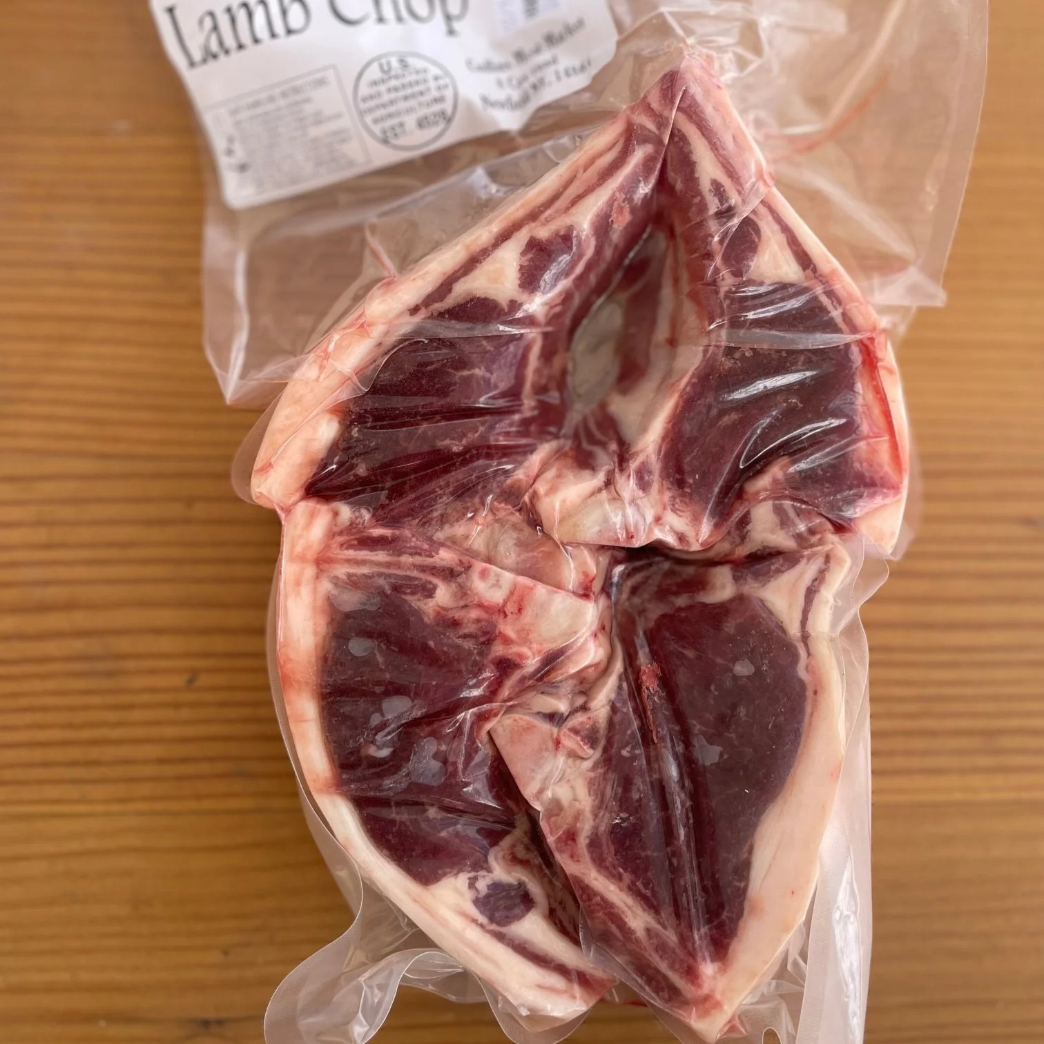 Vacuum-sealed lamb chops in plastic packaging on a wooden surface.