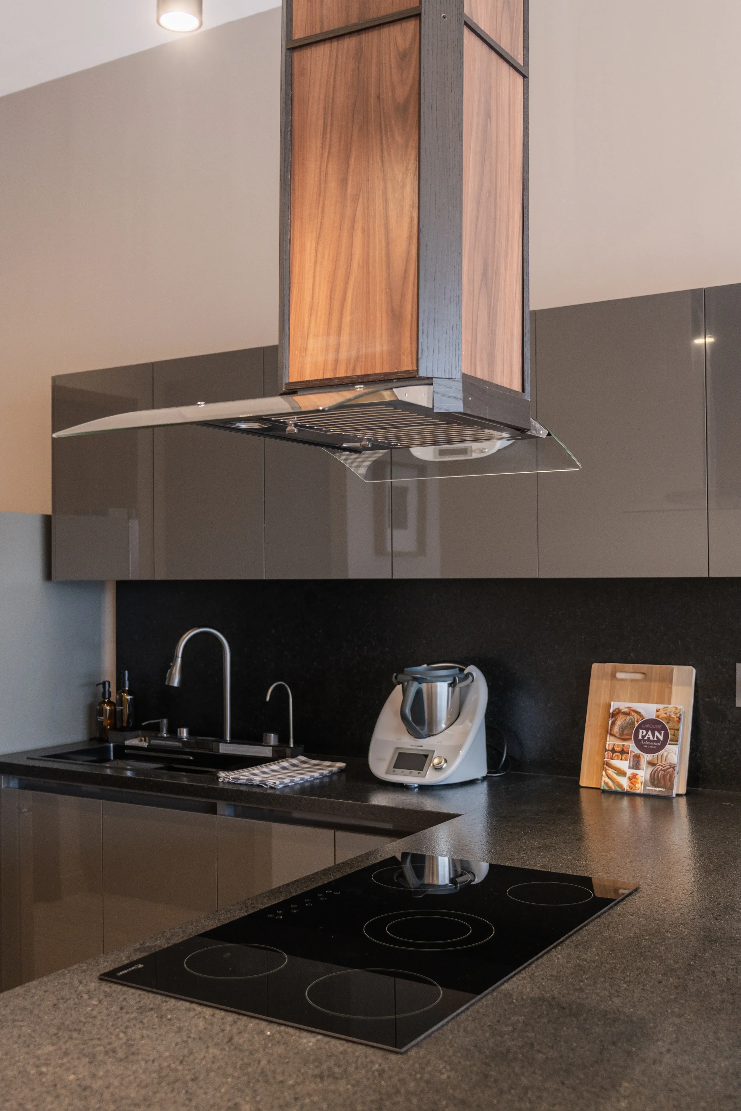 Modern kitchen with black countertop, gray cabinets, a stovetop, a backsplash, and a blender on the counter.