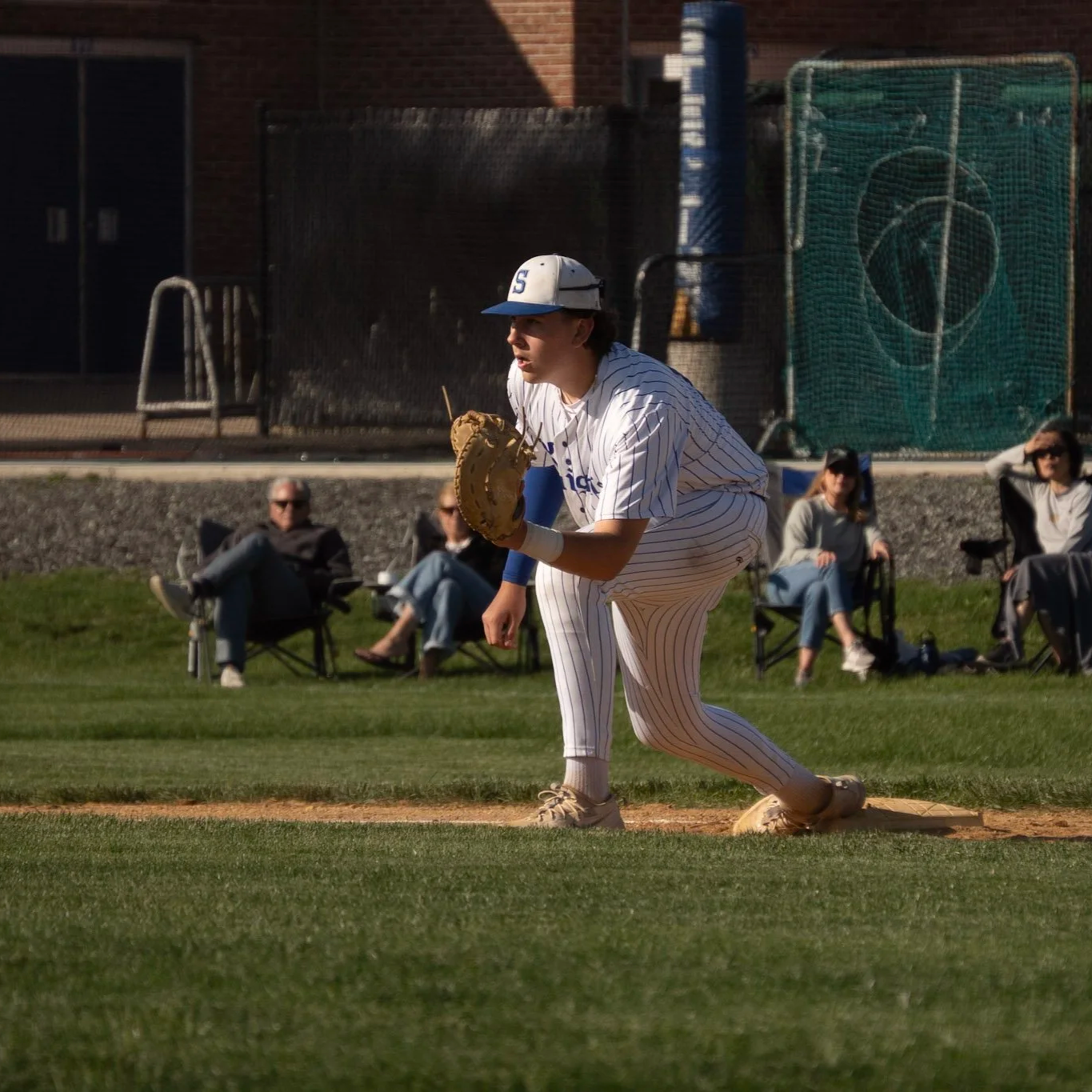 Baseball player in a striped uniform crouching on the field, ready to catch a ball, with spectators sitting and watching behind him.