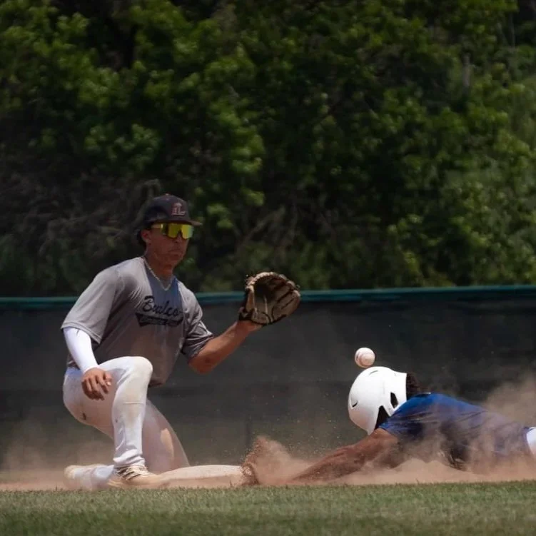 Baseball player sliding into a base as the opposing player catches the ball during a game.
