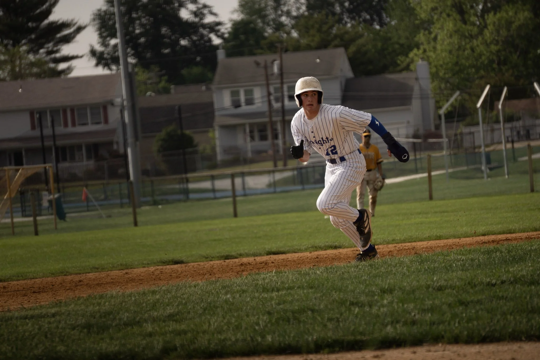 A baseball player in a white pinstripe uniform with the number 12, running on the base path with a helmet and gloves, on a baseball field during daytime.