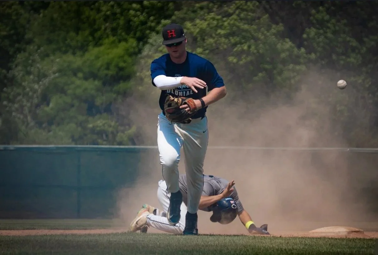 A baseball player catching a ball with a glove while another player falls on the ground in the background during a game.