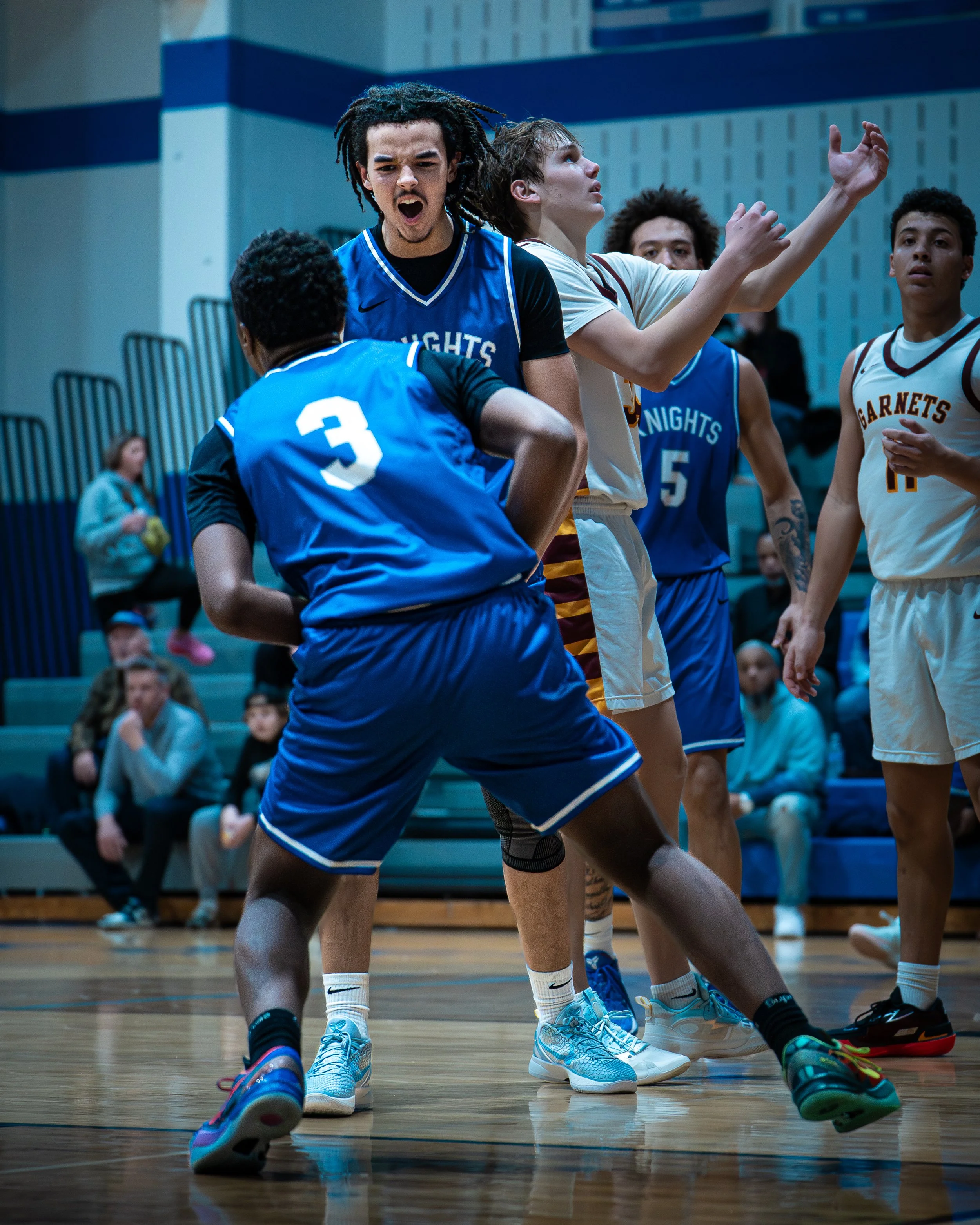 Young basketball players in a heated game on an indoor court, wearing blue and white jerseys, with spectators in the background.