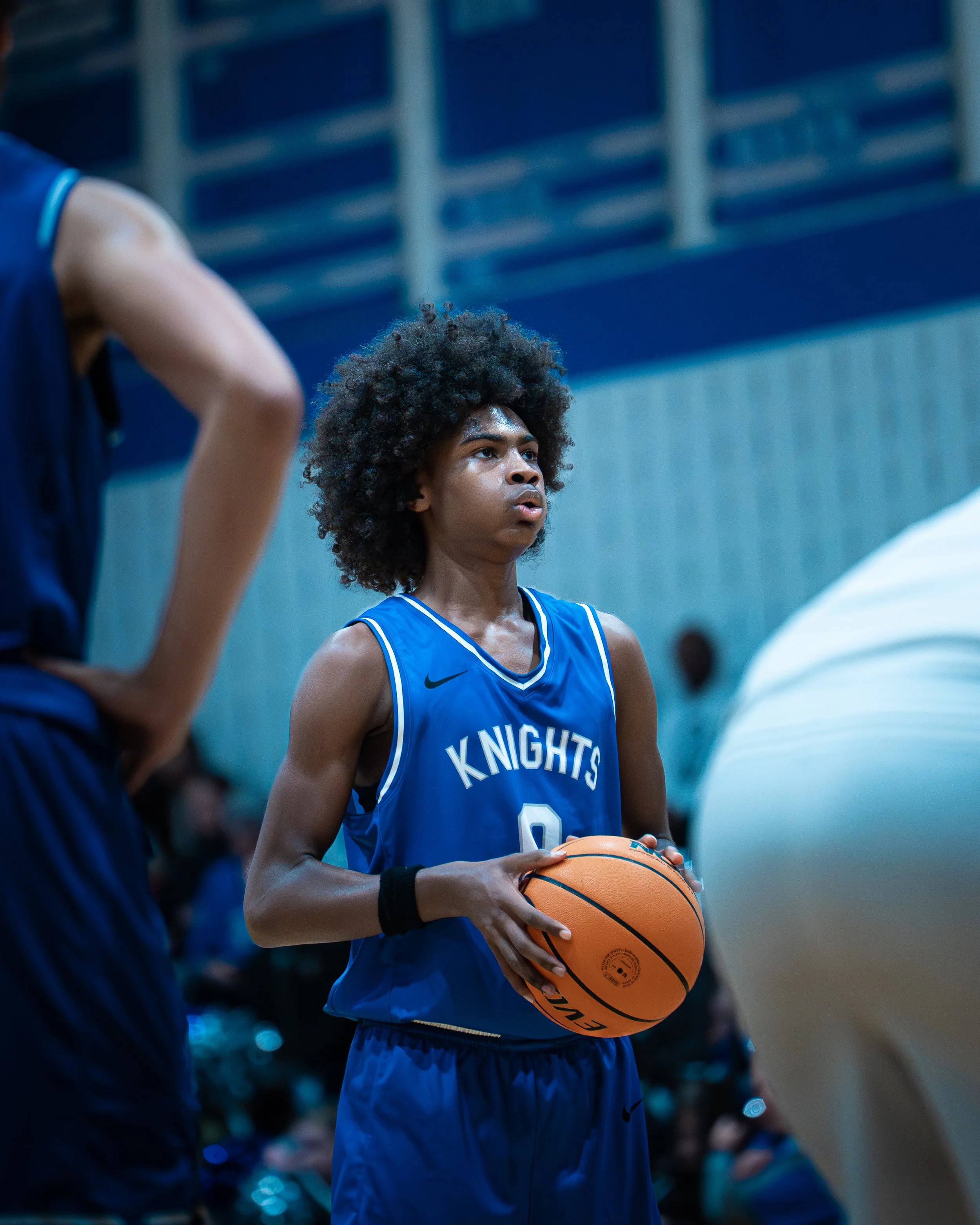 A female basketball player wearing a blue jersey with 'Knights' written on it, holding a basketball on a court during a game.
