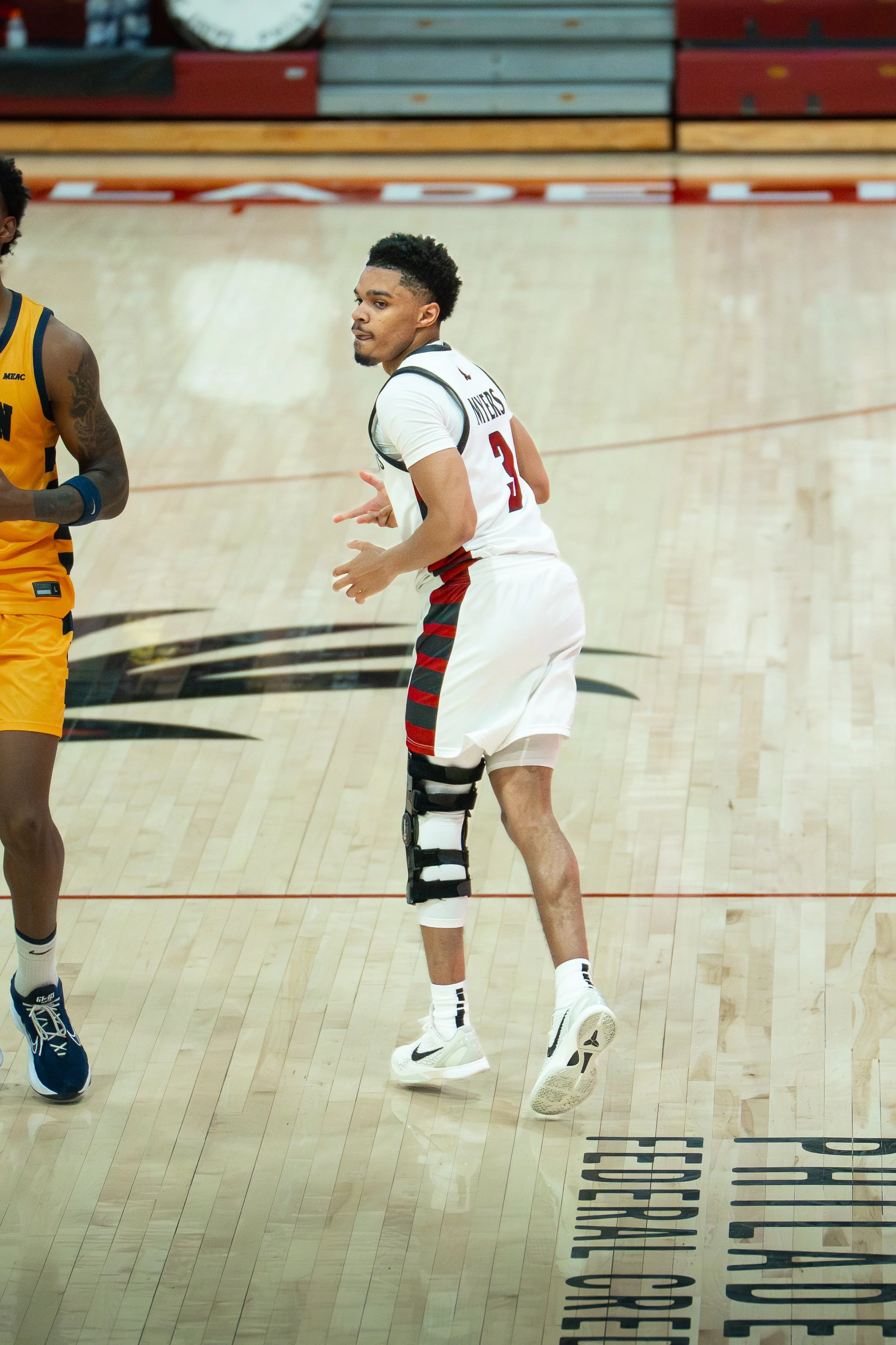 Basketball player in a white jersey with a black and red strap on his leg during a game.