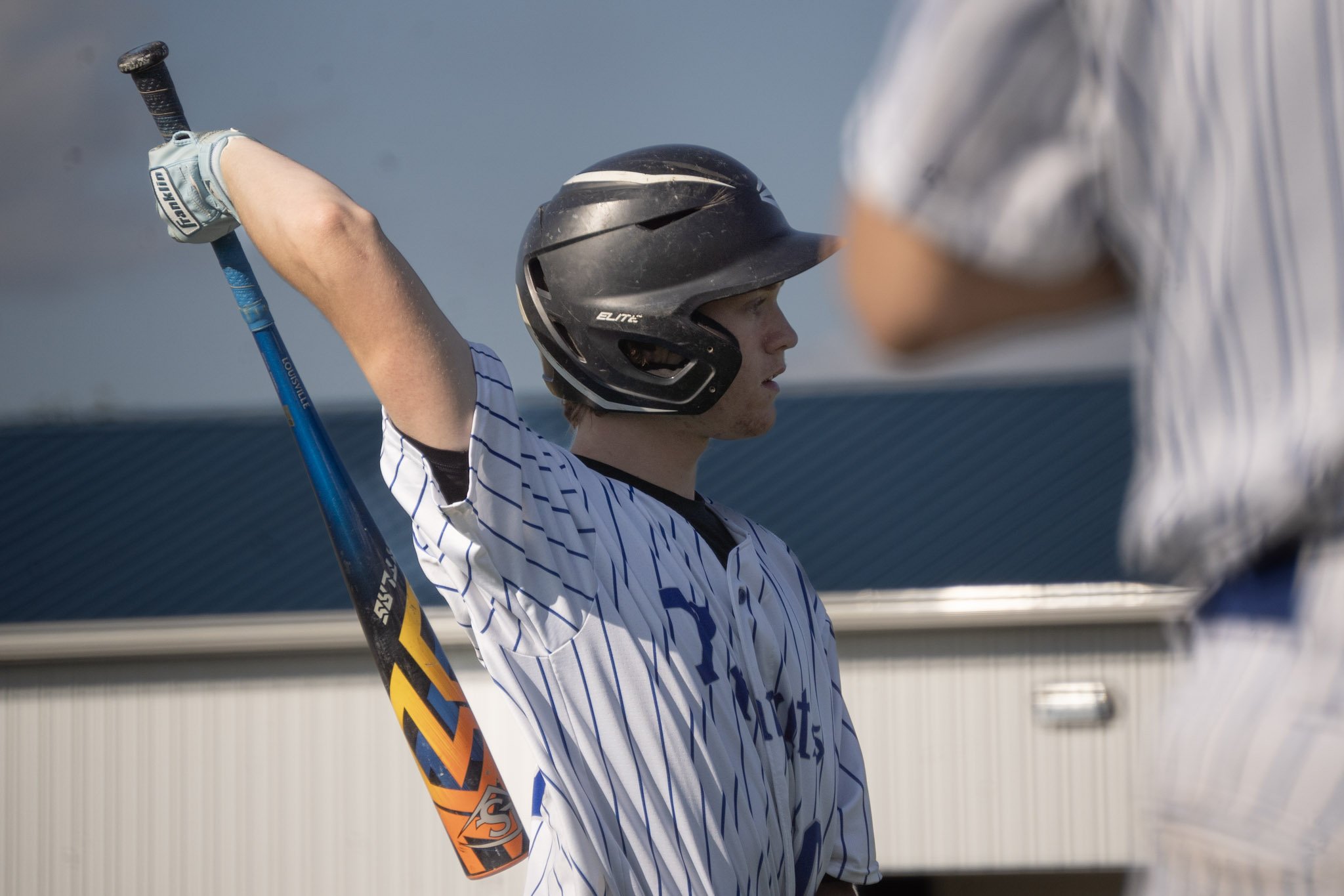 Young baseball player wearing a helmet, holding a bat, preparing for a swing, with a person in a striped shirt in the background.