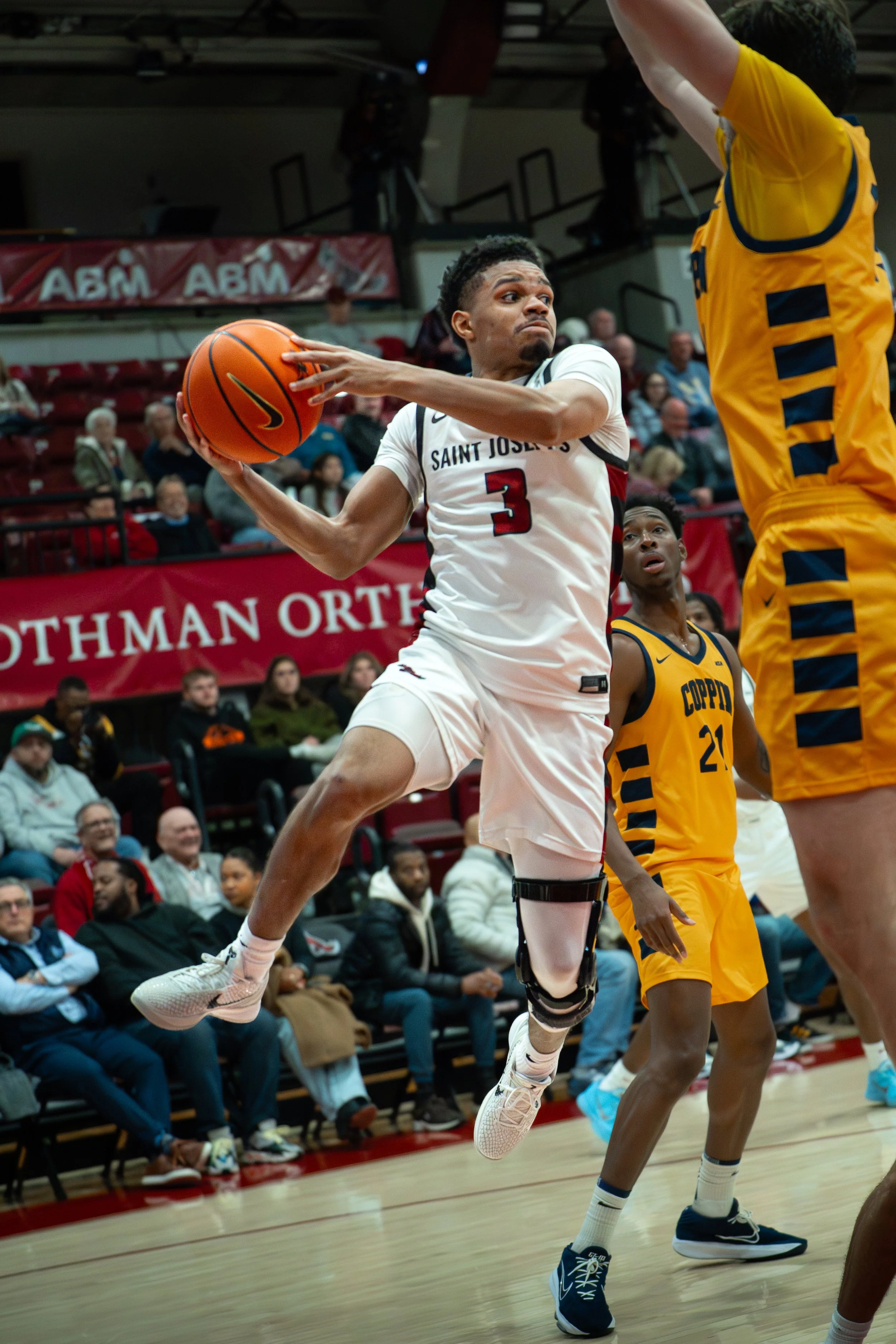 A basketball player in a white uniform jumping to make a play against defenders in yellow uniforms during a game.