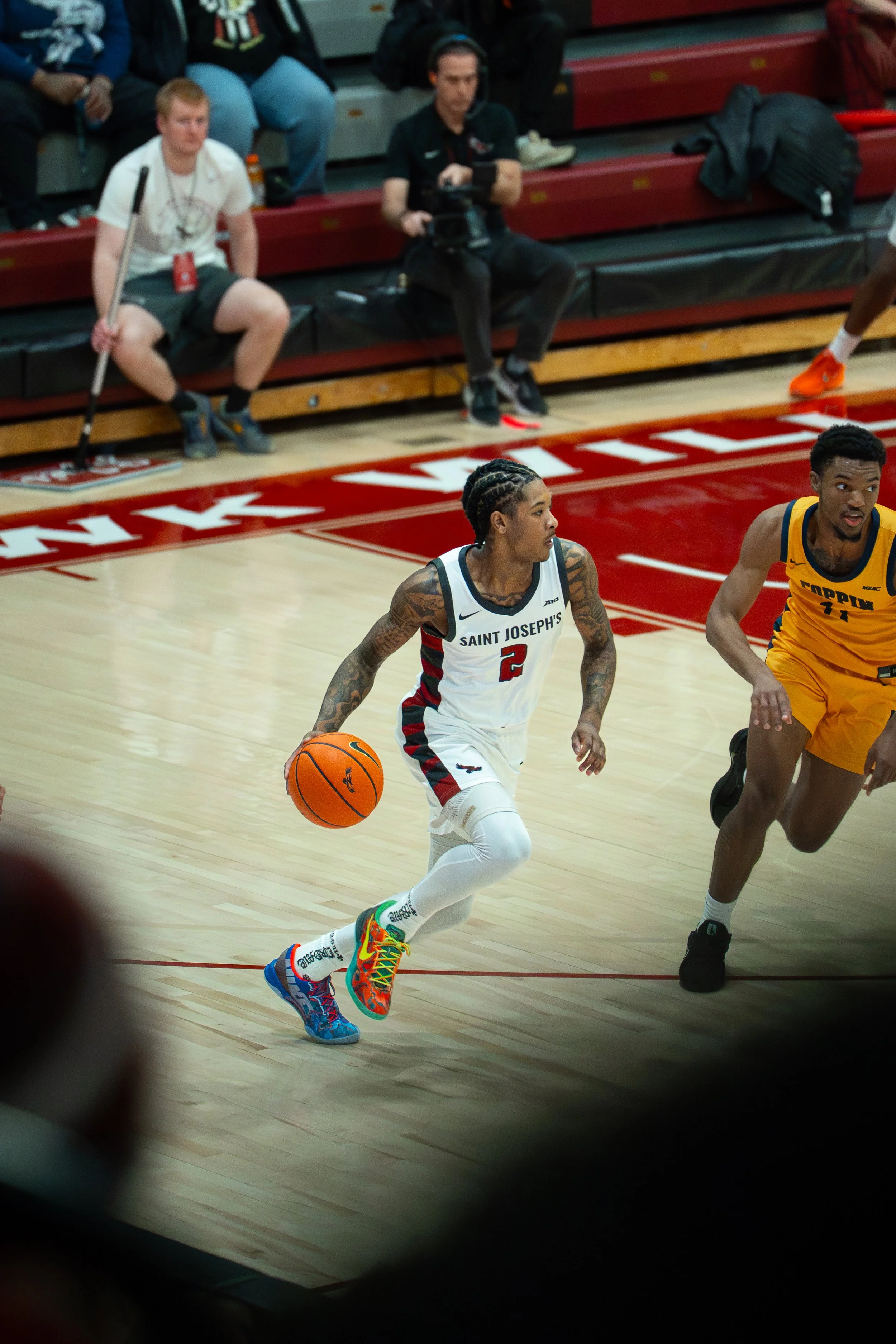 A basketball player in a white jersey with the number 2 dribbling the ball during a game, with another player in a yellow jersey nearby.