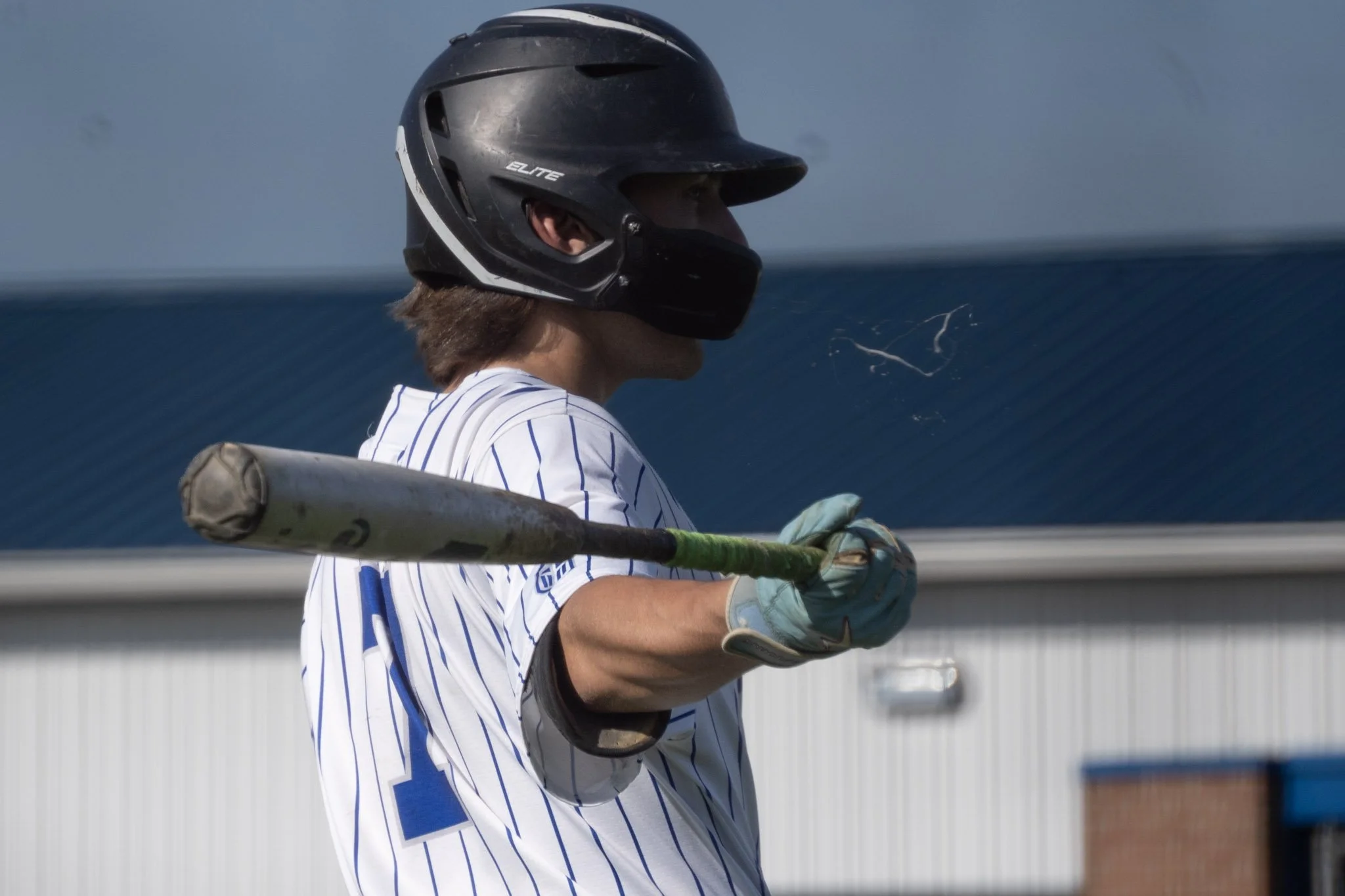 A baseball player in a pinstripe uniform holding a bat, wearing a black helmet and batting gloves, standing on the field.