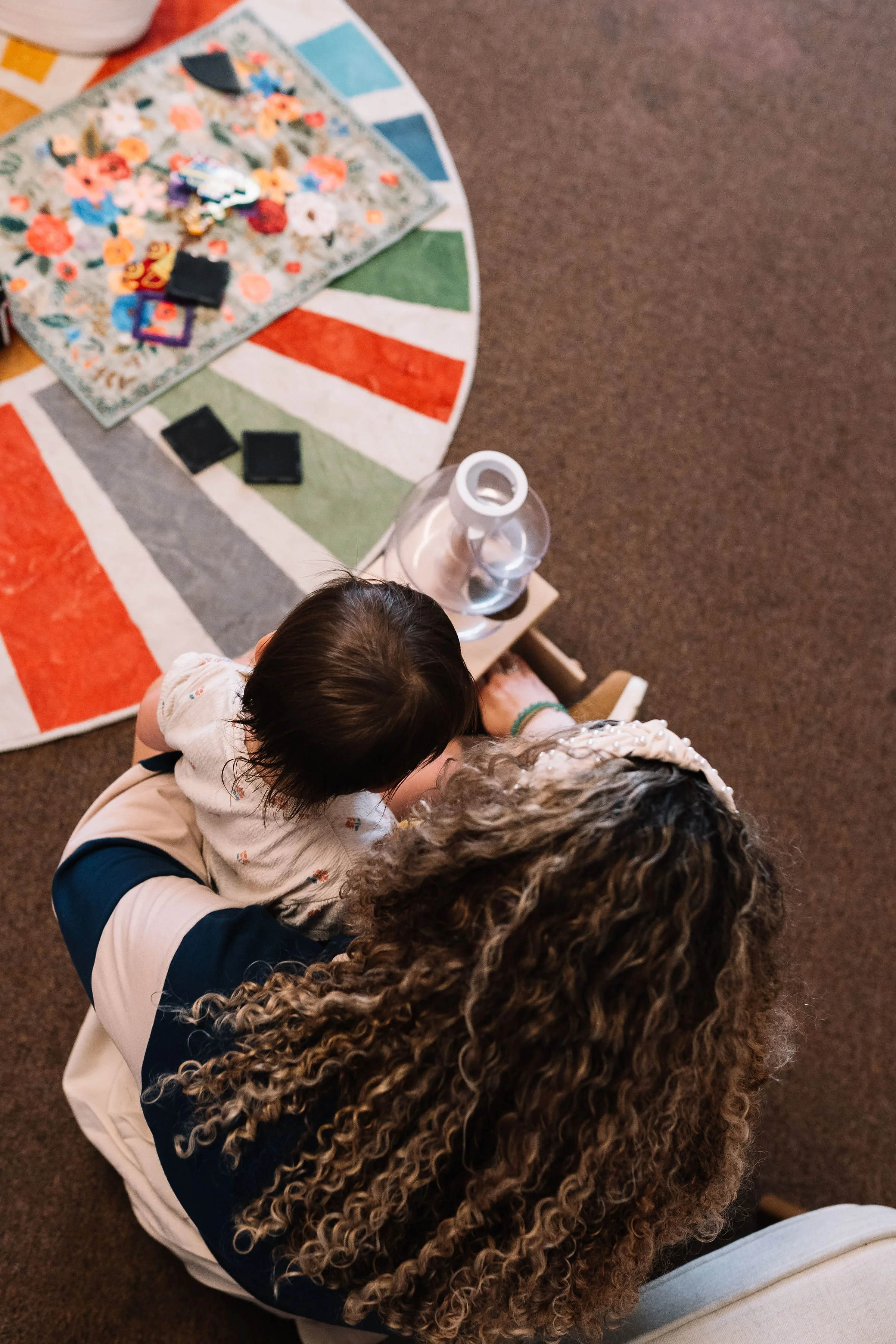 A woman with curly hair and a child with dark hair sit together on a chair, looking at a projector.