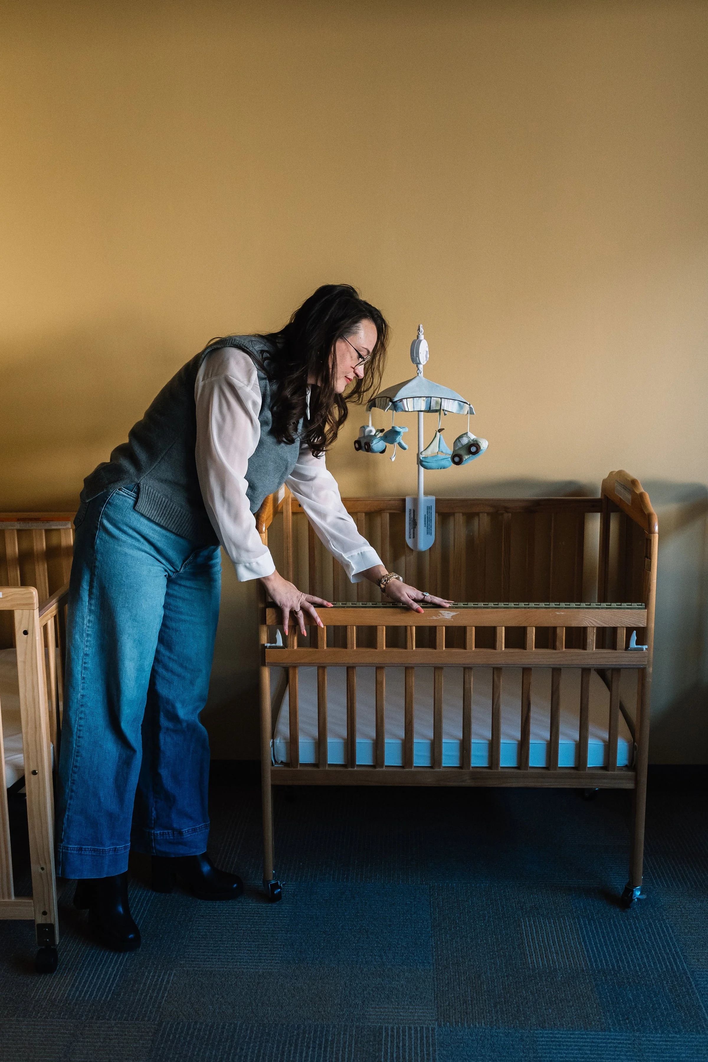 A woman leaning over a wooden crib with a mobile hanging above it in a nursery room.