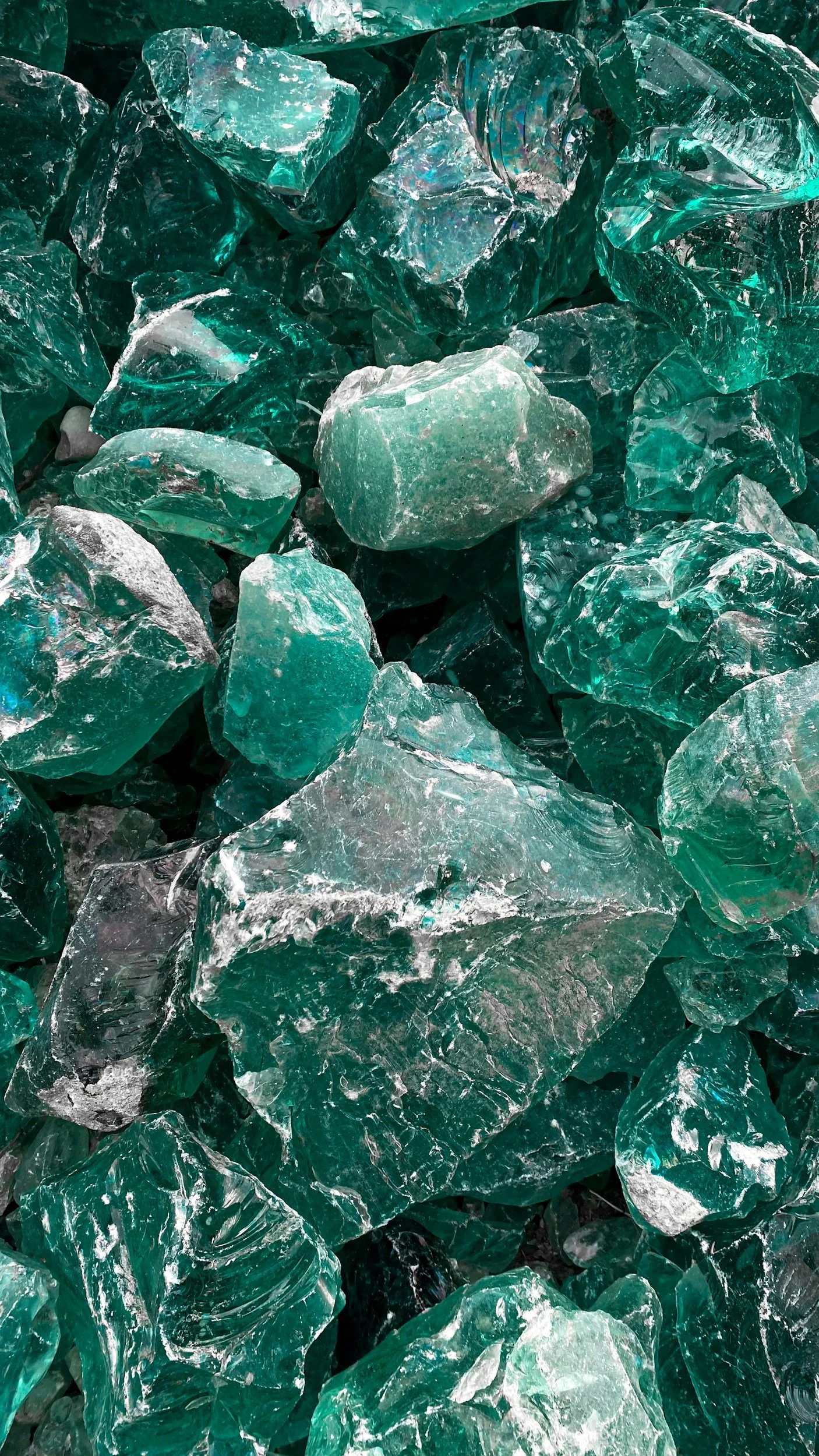 Close-up of shattered glass pieces in shades of teal and clear, with sharp edges and reflective surfaces.
