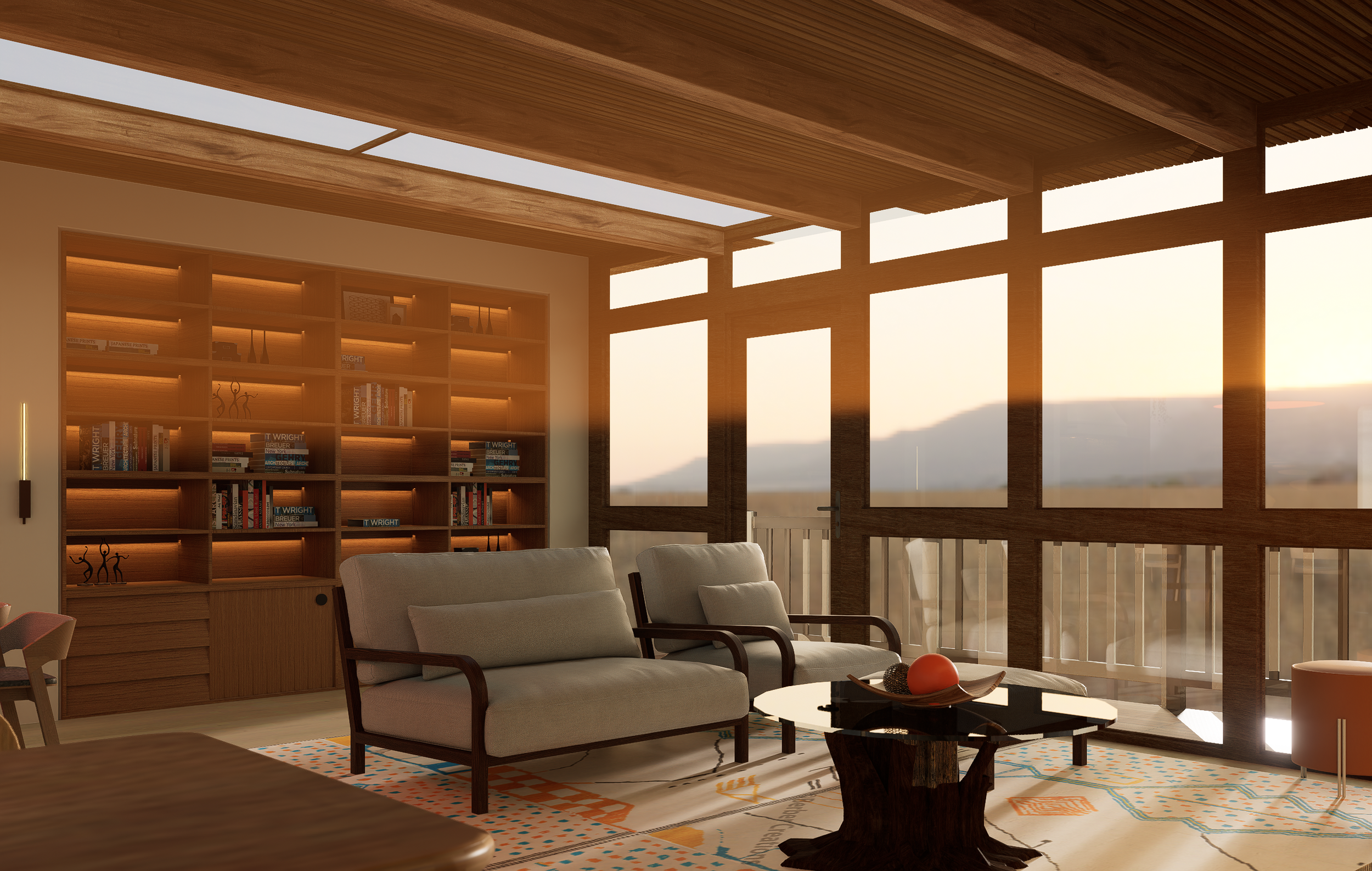 Living room with large windows showing a sunset view, two beige sofas with wooden arms, a black coffee table with decorative objects, a colorful area rug, a wooden bookshelf with books and sculptures, and warm lighting.