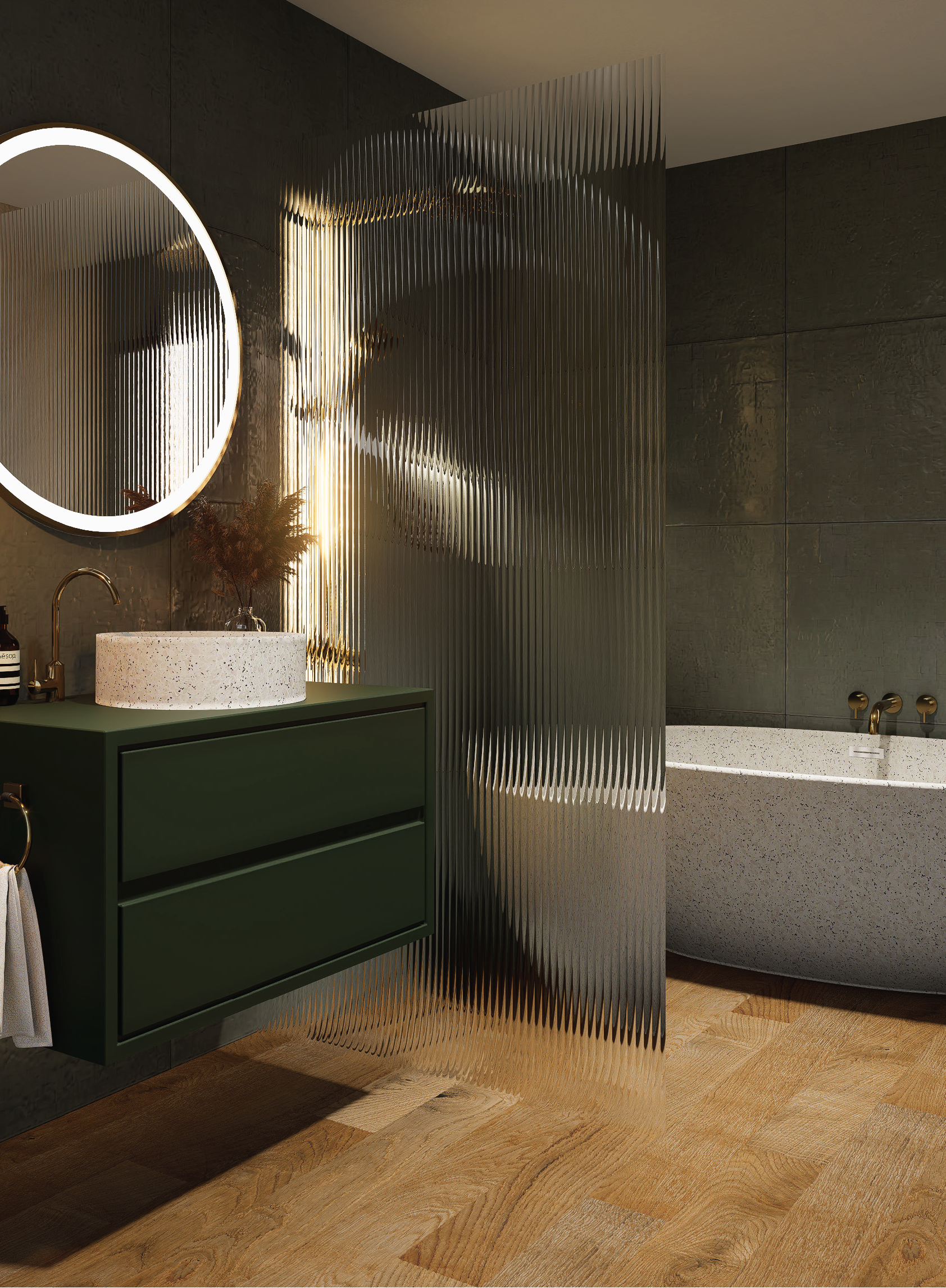Modern bathroom with a green vanity, speckled vessel sink, round illuminated mirror, decorative plant, textured metallic partition, and freestanding terrazzo bathtub against dark wall tiles and wood flooring.