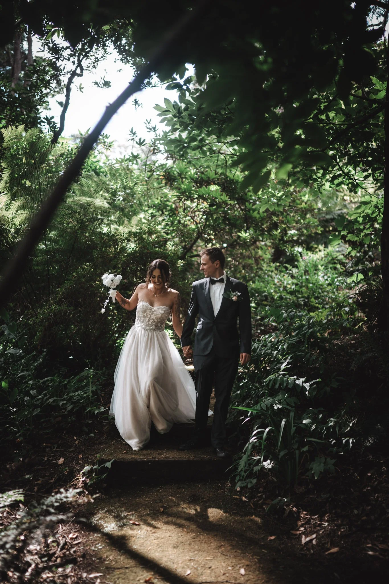 A bride and groom walking hand-in-hand through a lush, green forest during their wedding.