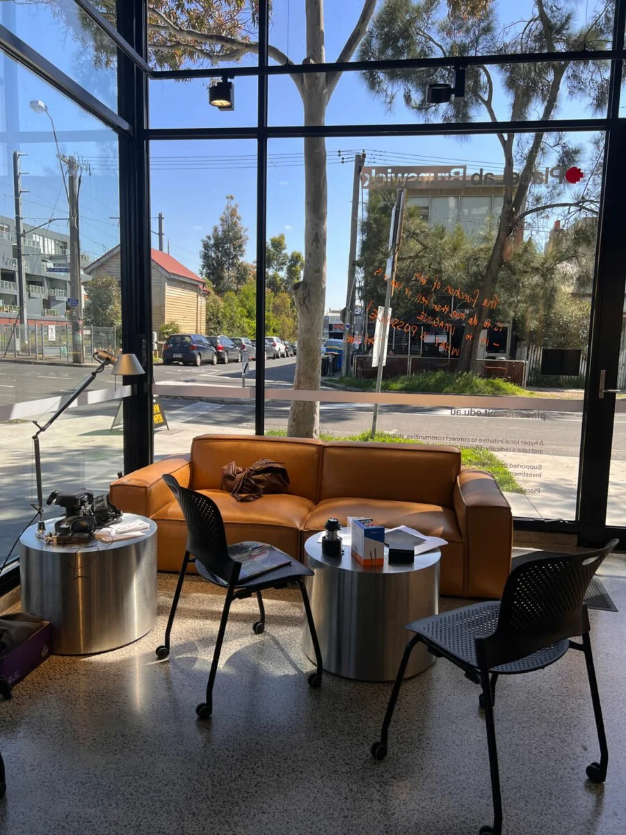 A corner of the office, feature glass walls, a brown leather couch, and a couple of chairs and side tables.