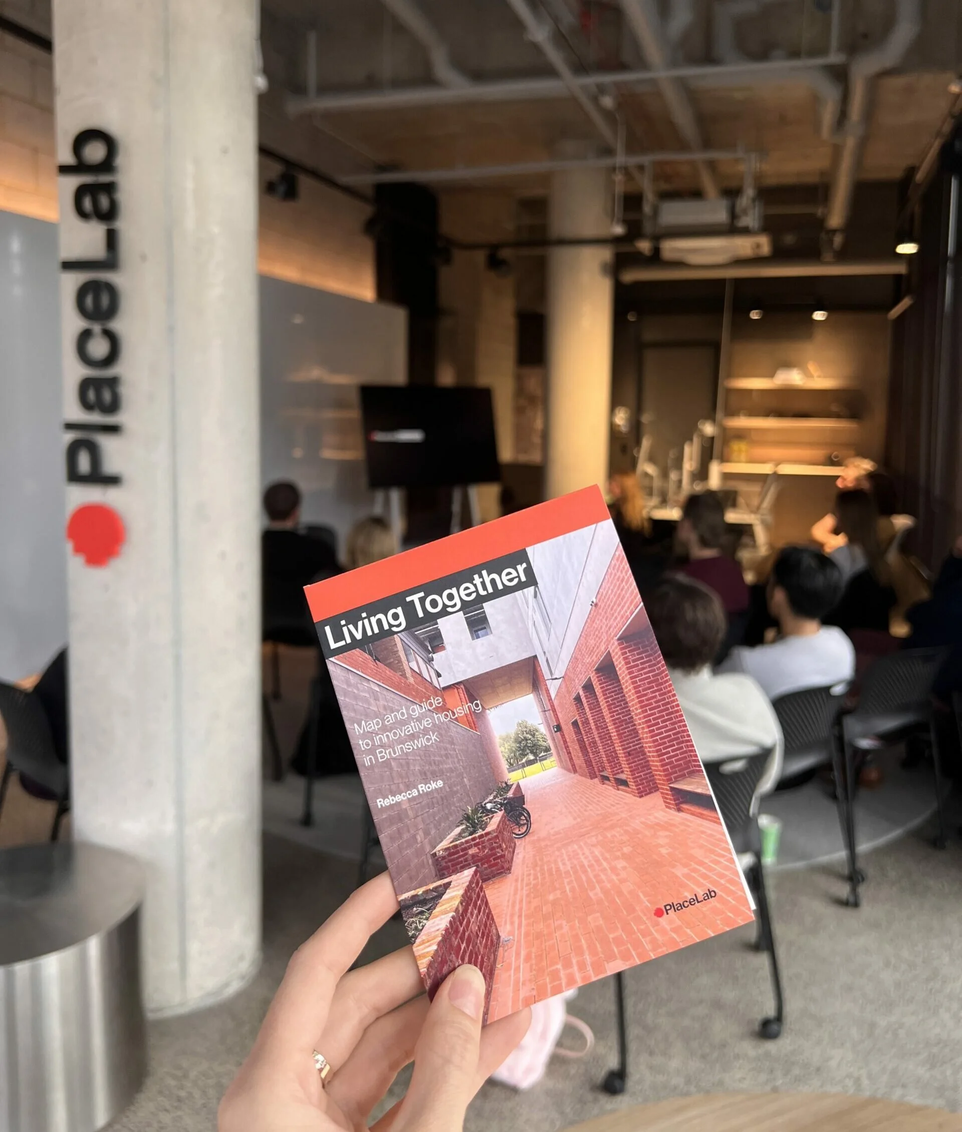 A small booklet, titled Living Together, is held in front of a cement pillar.