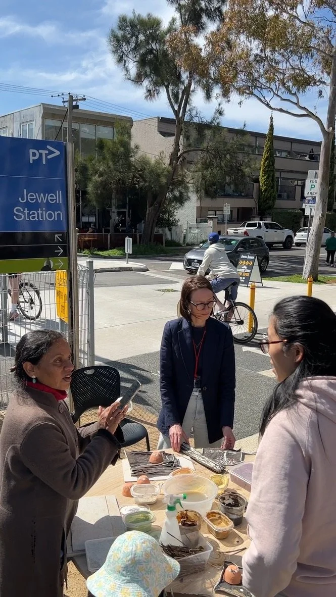 Three women around a table outside by Jewell train station, with paints on the table.