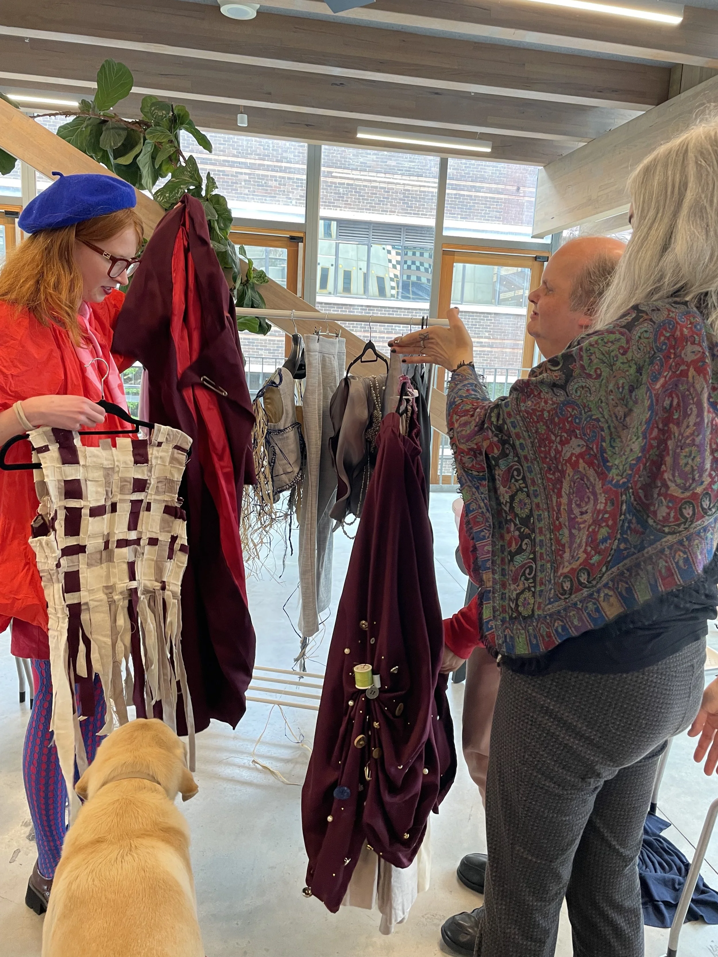 A fashion student wearing a blue beret holds a garment woven of strips of fabrics to show a person who is blind.
