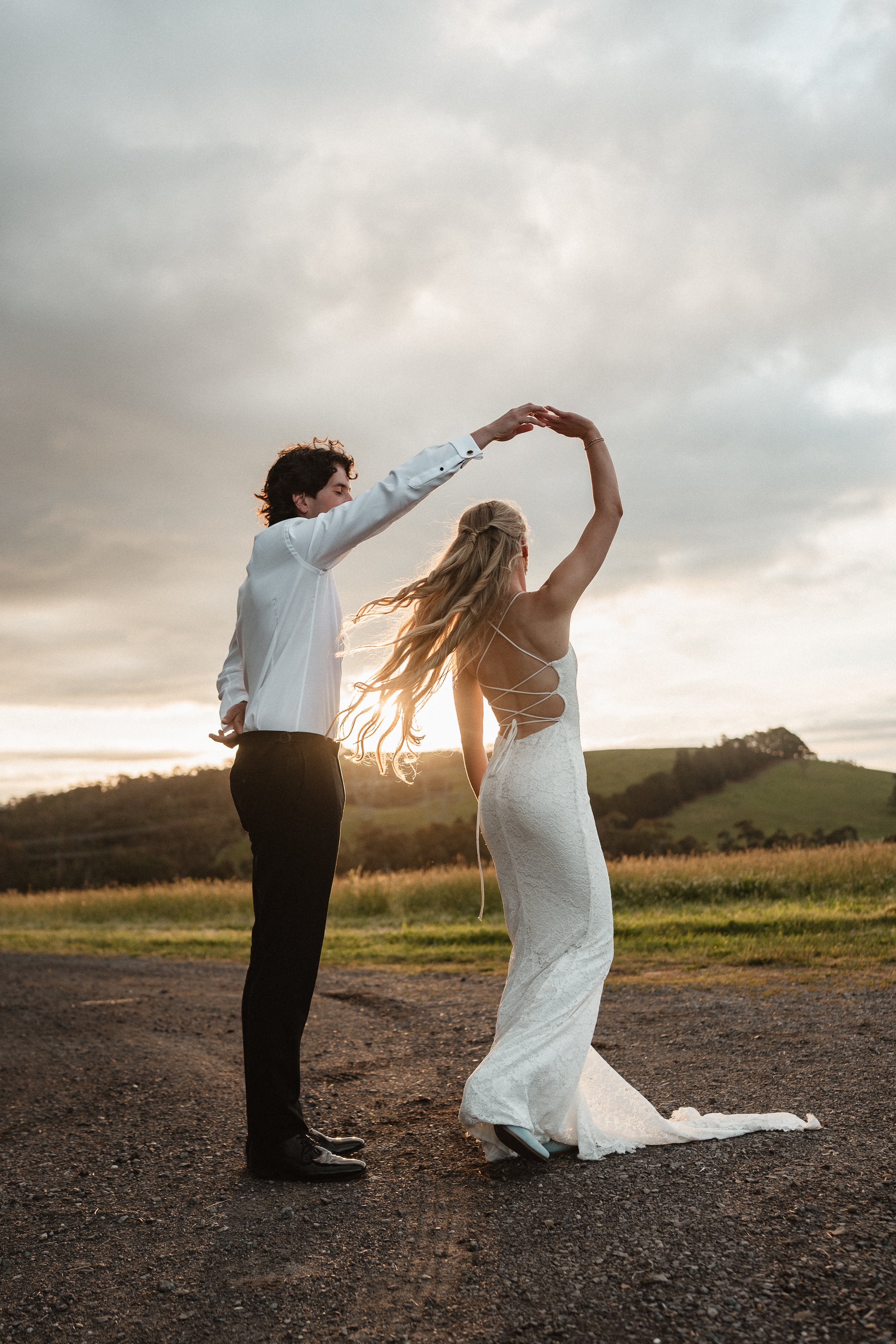 A couple dancing outdoors in a field at sunset, with rolling hills in the background.