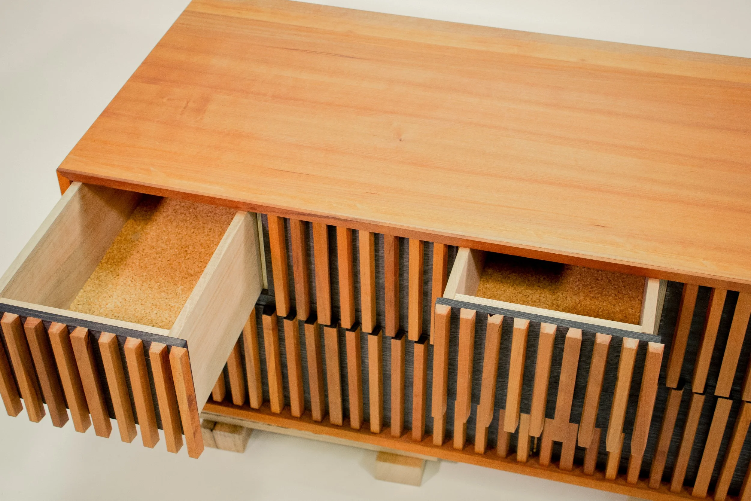 A collection of wooden furniture pieces, including open drawers with a light-colored interior, and a slatted part, all placed on a light-colored surface.