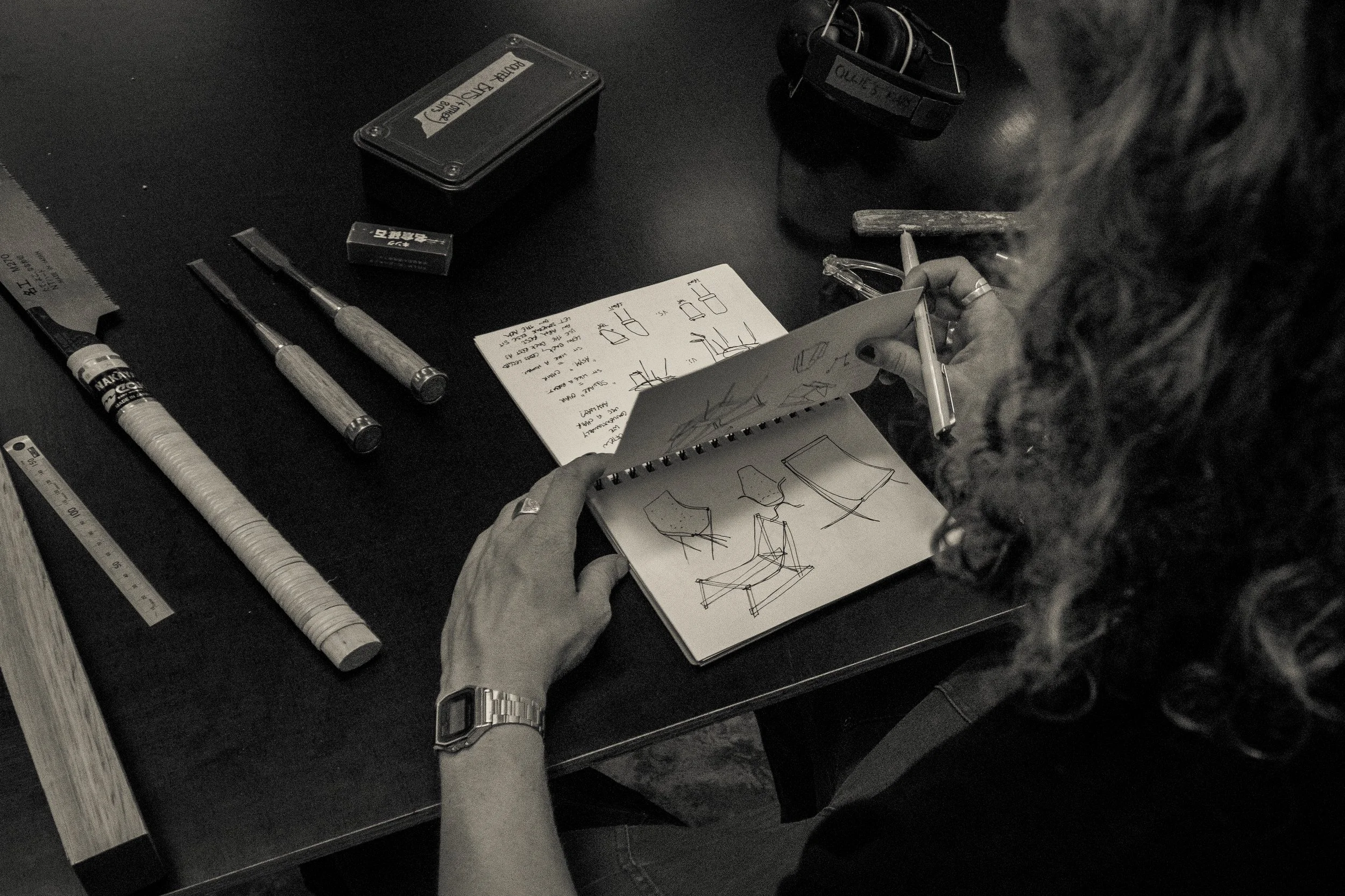 Person working with sketches and tools on a black table, surrounded by various drawing and measuring tools.