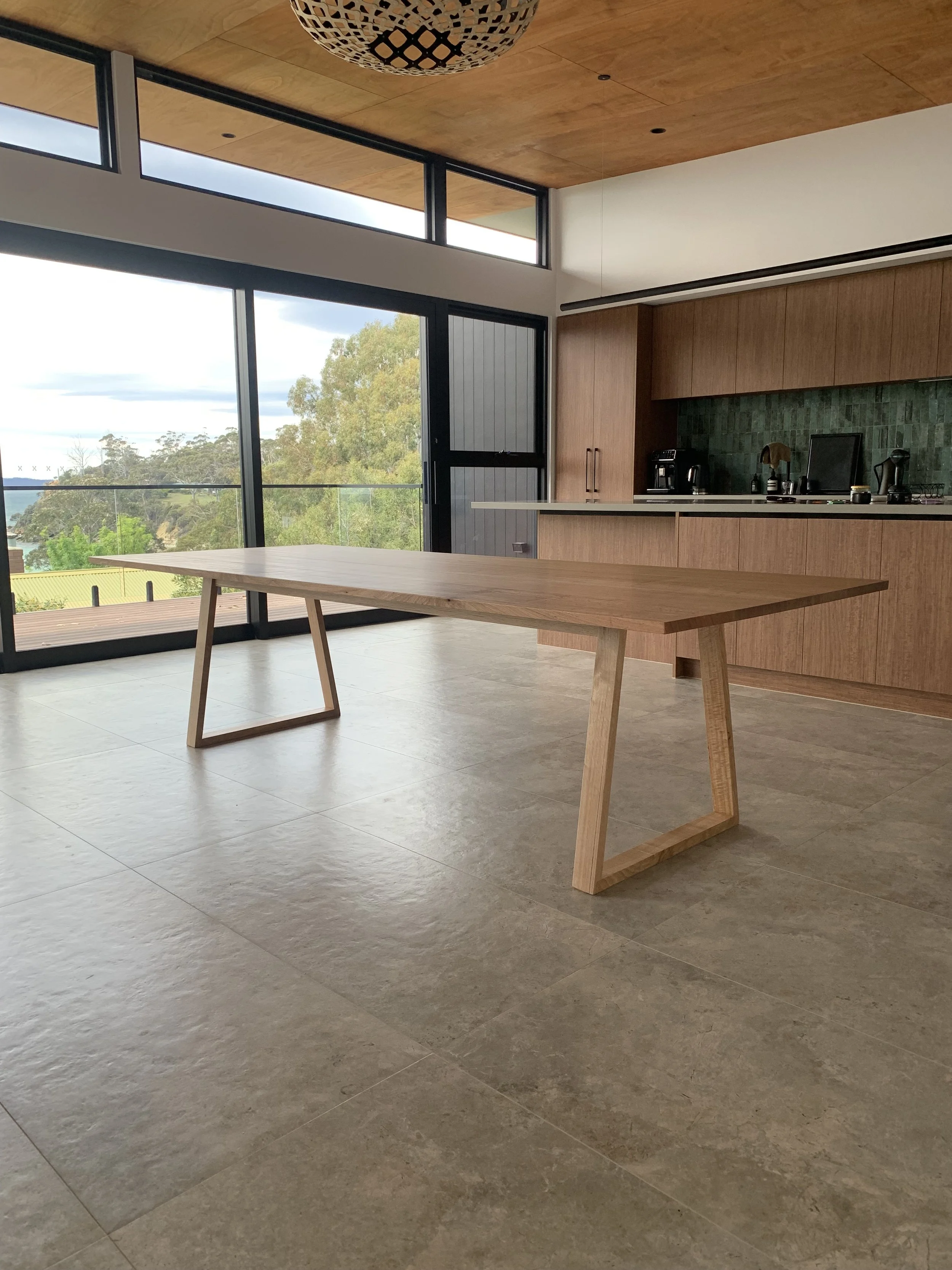 Modern kitchen with large sliding glass doors, wooden cabinets, a green tiled backsplash, and a wooden table in the foreground.