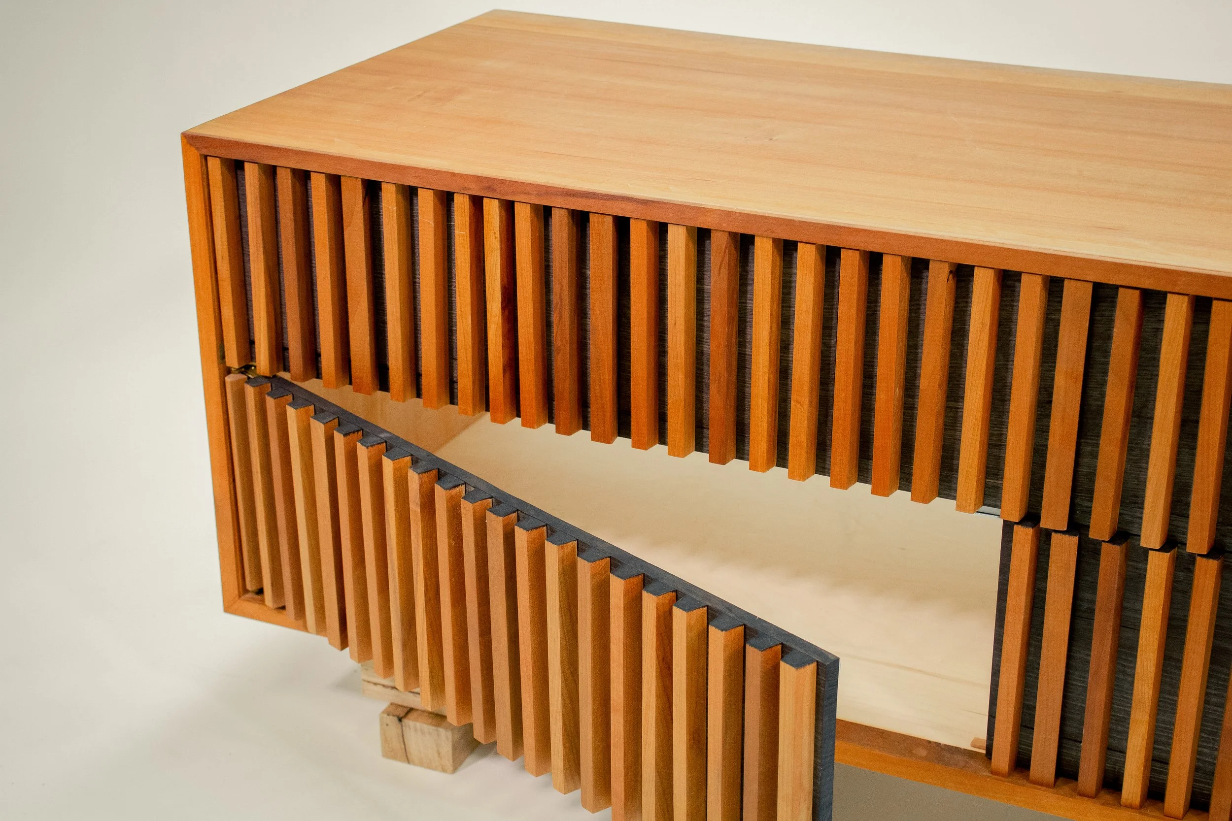 Two wooden slatted cabinets, one placed on top of the other, with a light-colored top surface, against a plain wall.
