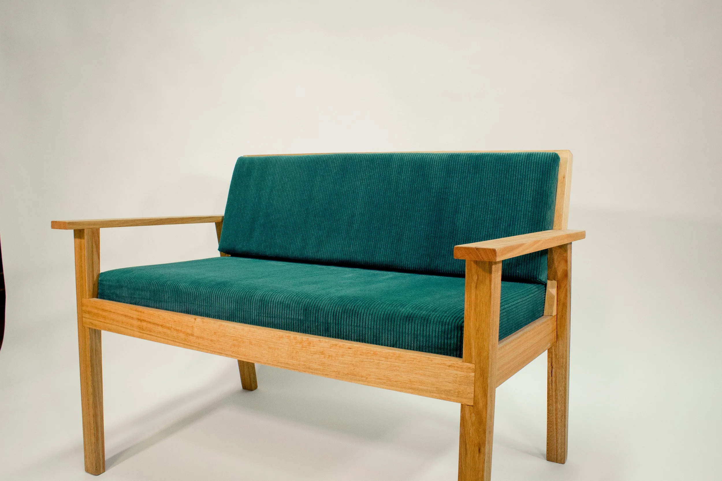 A wooden bench with green cushions on a plain white background.