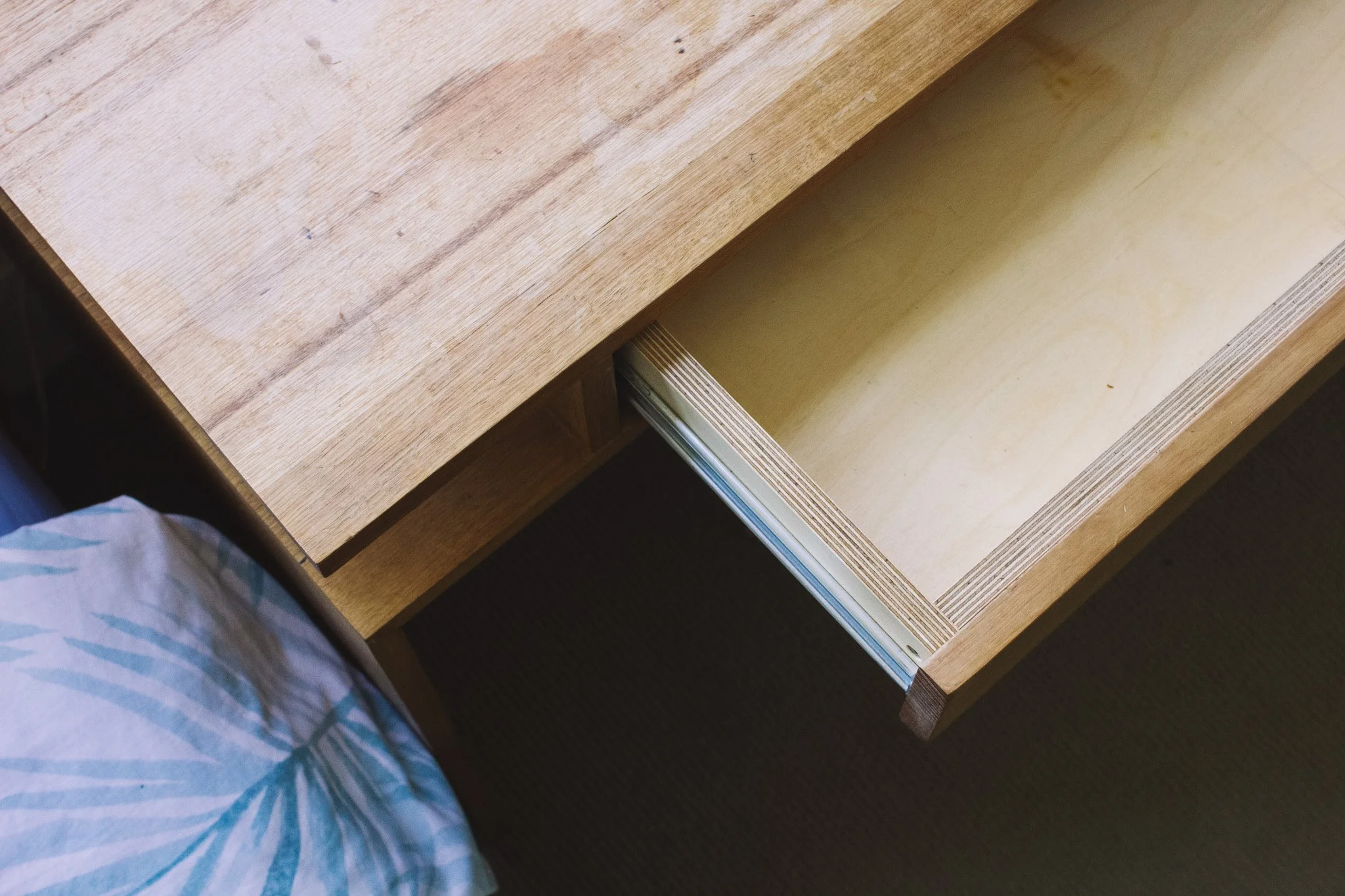A wooden desk with a drawer partially pulled out, viewed from above. Part of a person wearing checkered pajamas is visible in the lower left corner.