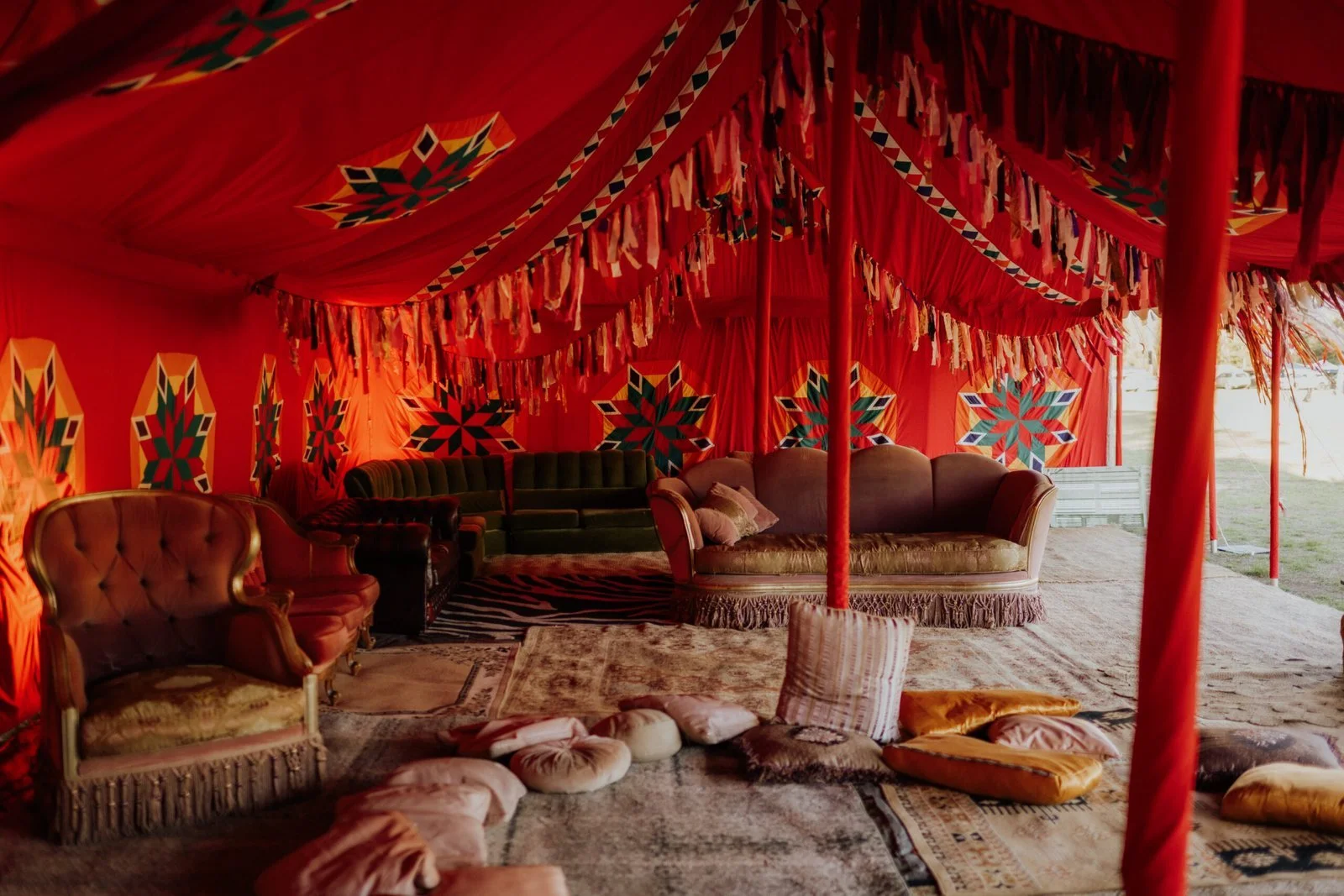 Leisure Disco Decor creates decorative tent interior with red fabric walls and ceiling, colorful geometric patterns, vintage-style sofas, and floor cushions, set outdoors.